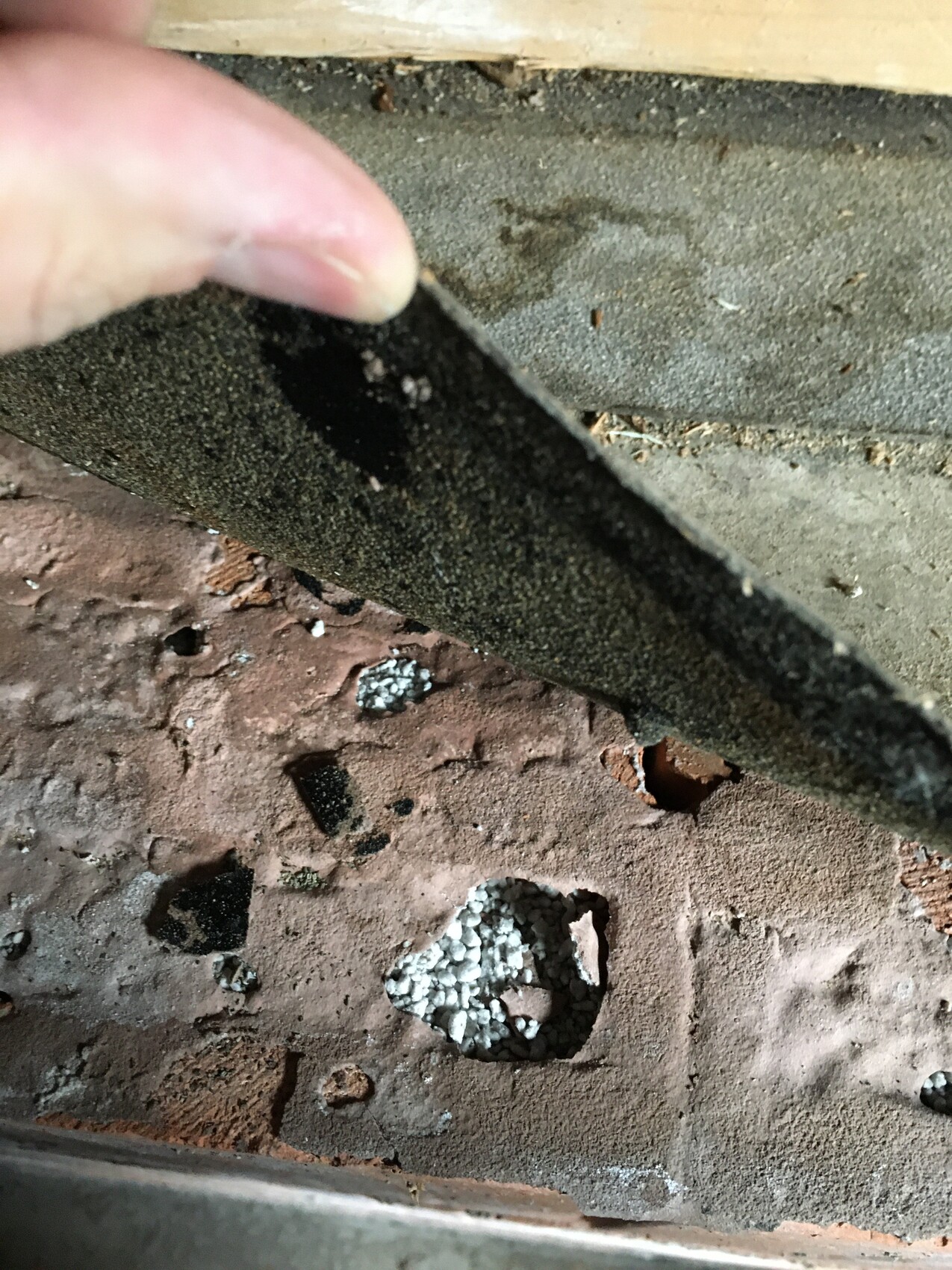 Hand hebt eine schwarze, raue Isolationsplatte von rotem Ziegelboden ab; darunter weißer Kies.