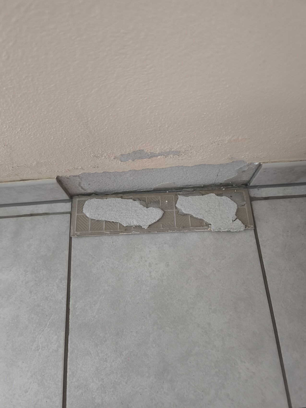 Wandfußbereich mit abplatzendem Putz, beschädigter Sockel und Fliesenboden sichtbar.