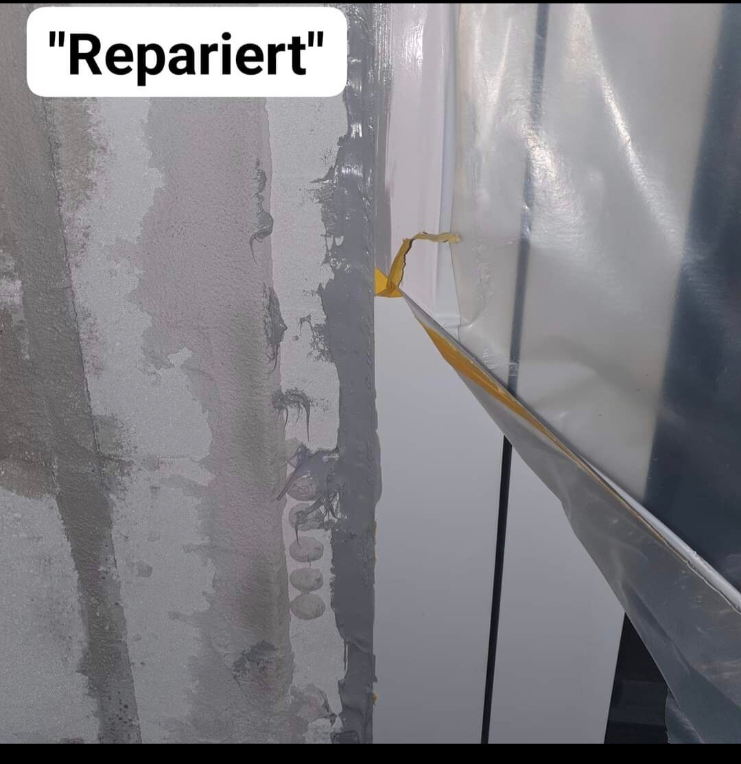 Reparierte Wandfläche: Putzschäden links neben Silberfolie und gelbem Klebeband.