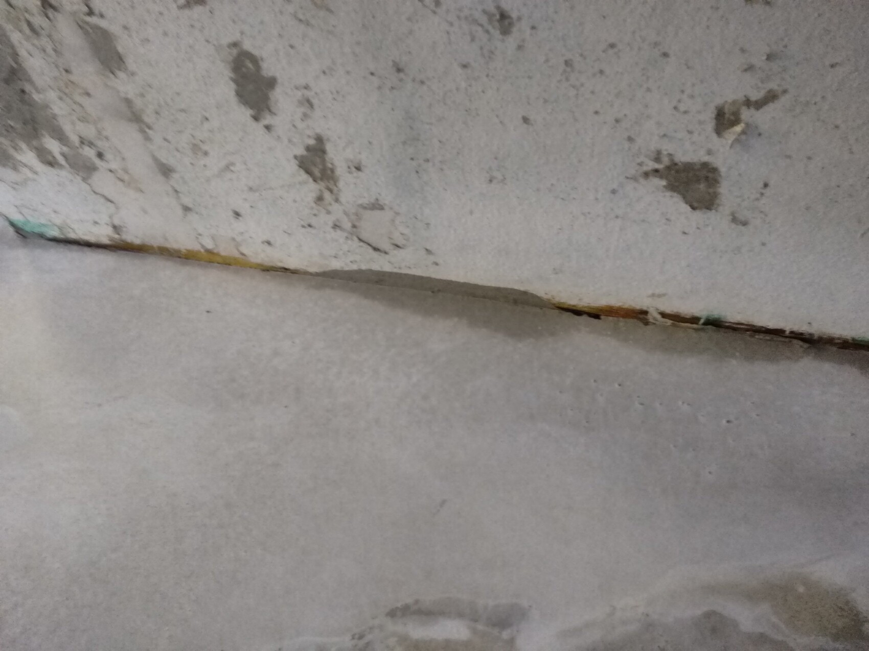 Rissige Wand- und Bodenstelle im Keller mit abgeblättertem Putz.