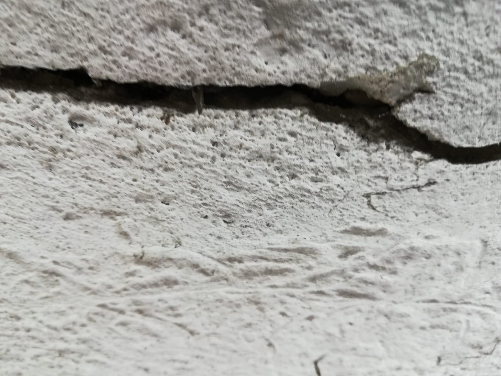 Riss in rauer Betonwand mit unregelmäßiger Oberfläche.