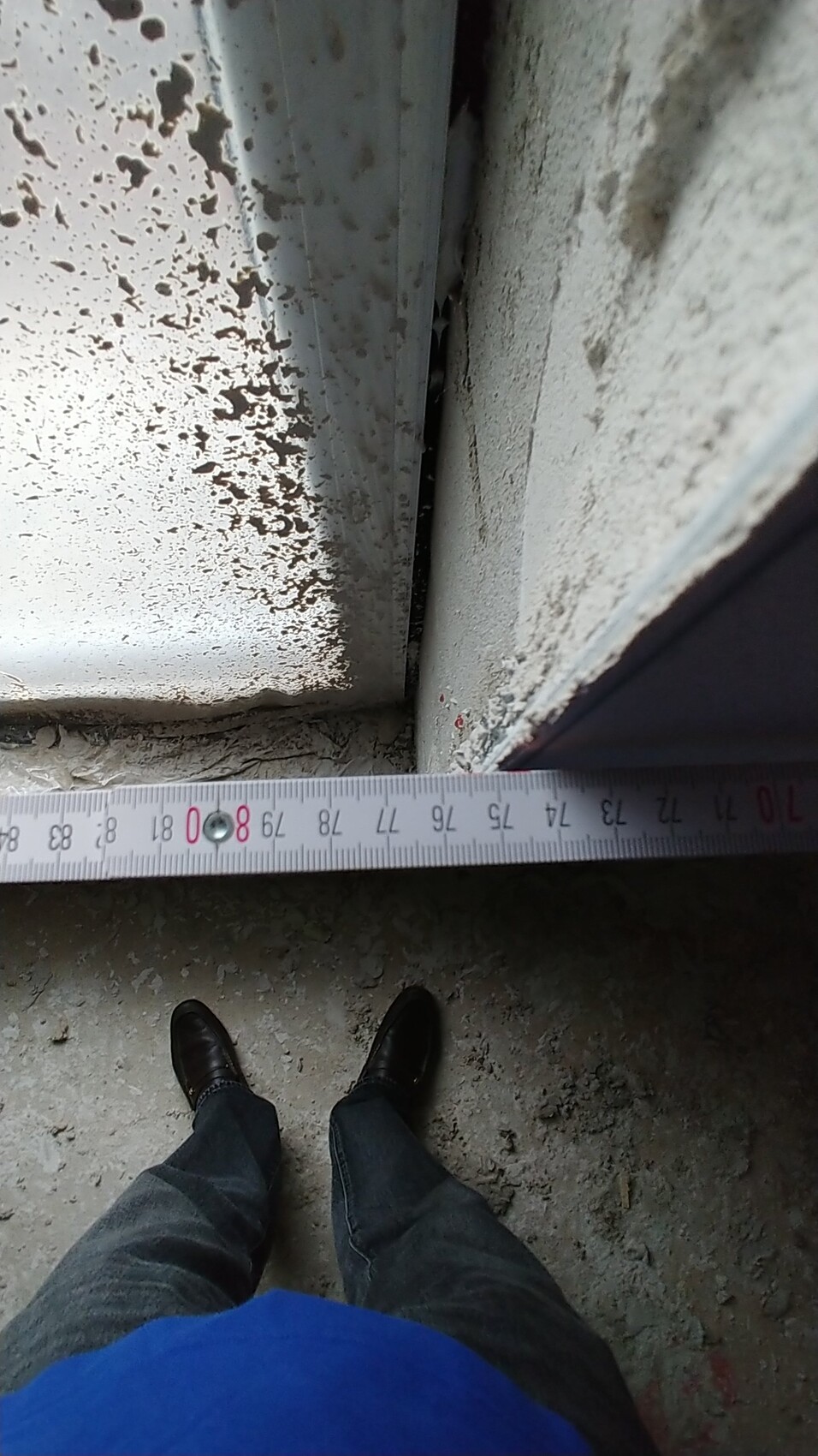 Person steht auf Baustelle neben rostiger Metalloberfläche mit abblätternder Farbe und Messband