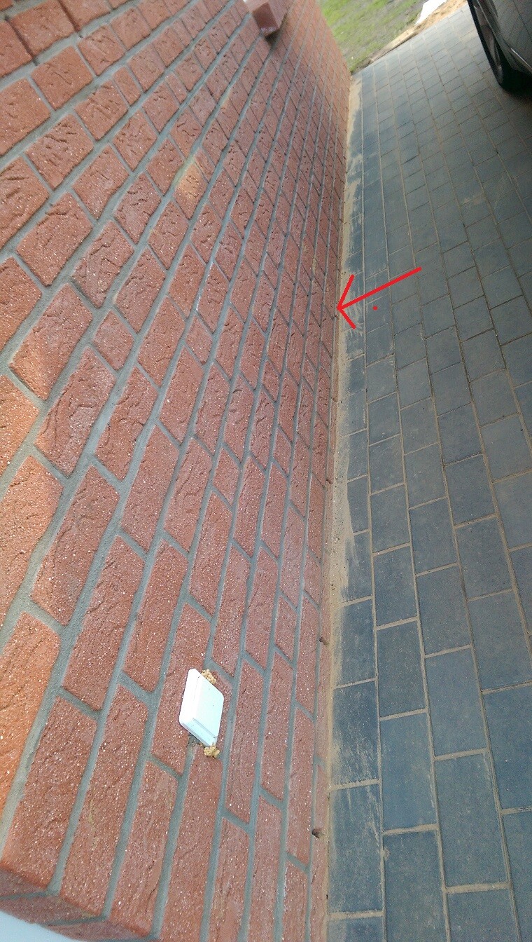 Außenwand aus roten Ziegeln neben grauer Pflasterfläche; sichtbare Fuge zwischen Wand und Boden