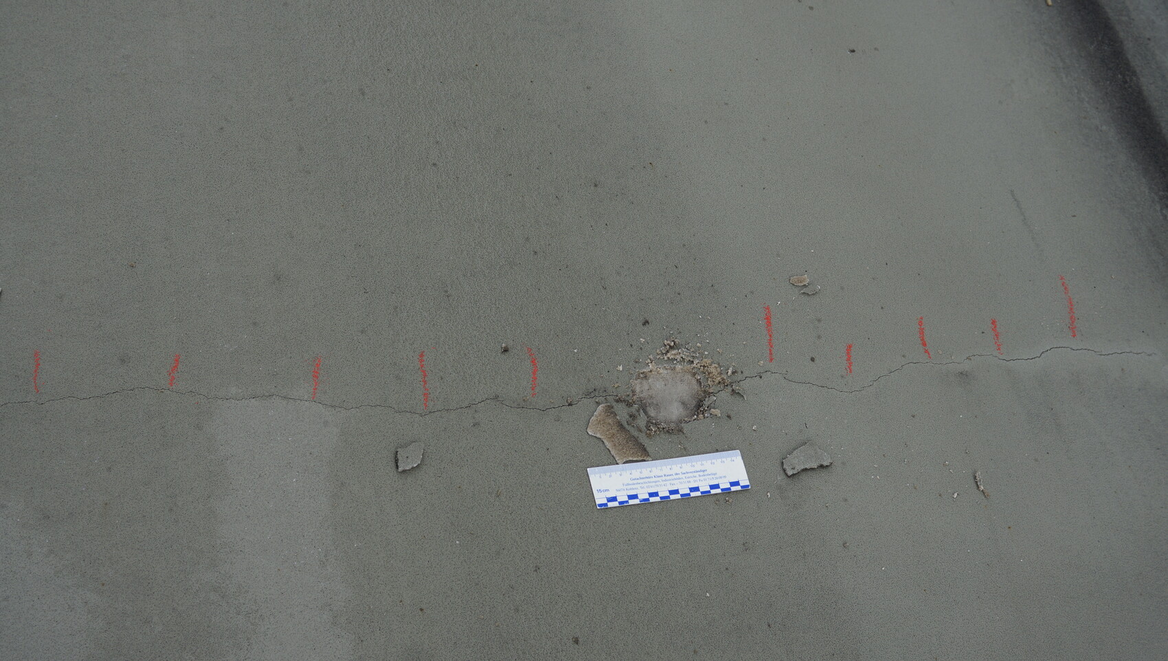 Betonplatte mit sichtbarem Riss, Messskala und Bauteilresten