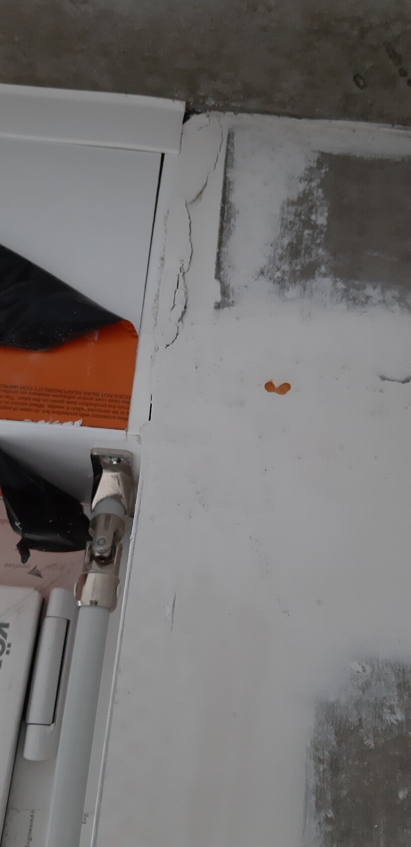 Türrahmen mit Rissen im Putz, sichtbares Scharnier und orange Verpackung im Spalt
