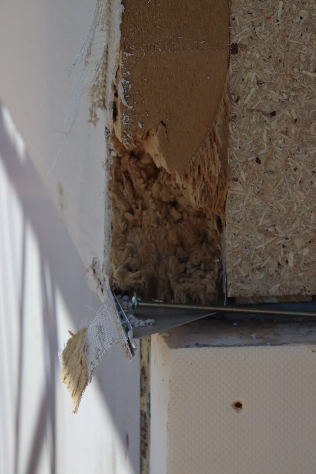Beschädigte Dämmung in Wandöffnung; braunes Material zwischen OSB-Platten, Rohr darunter.