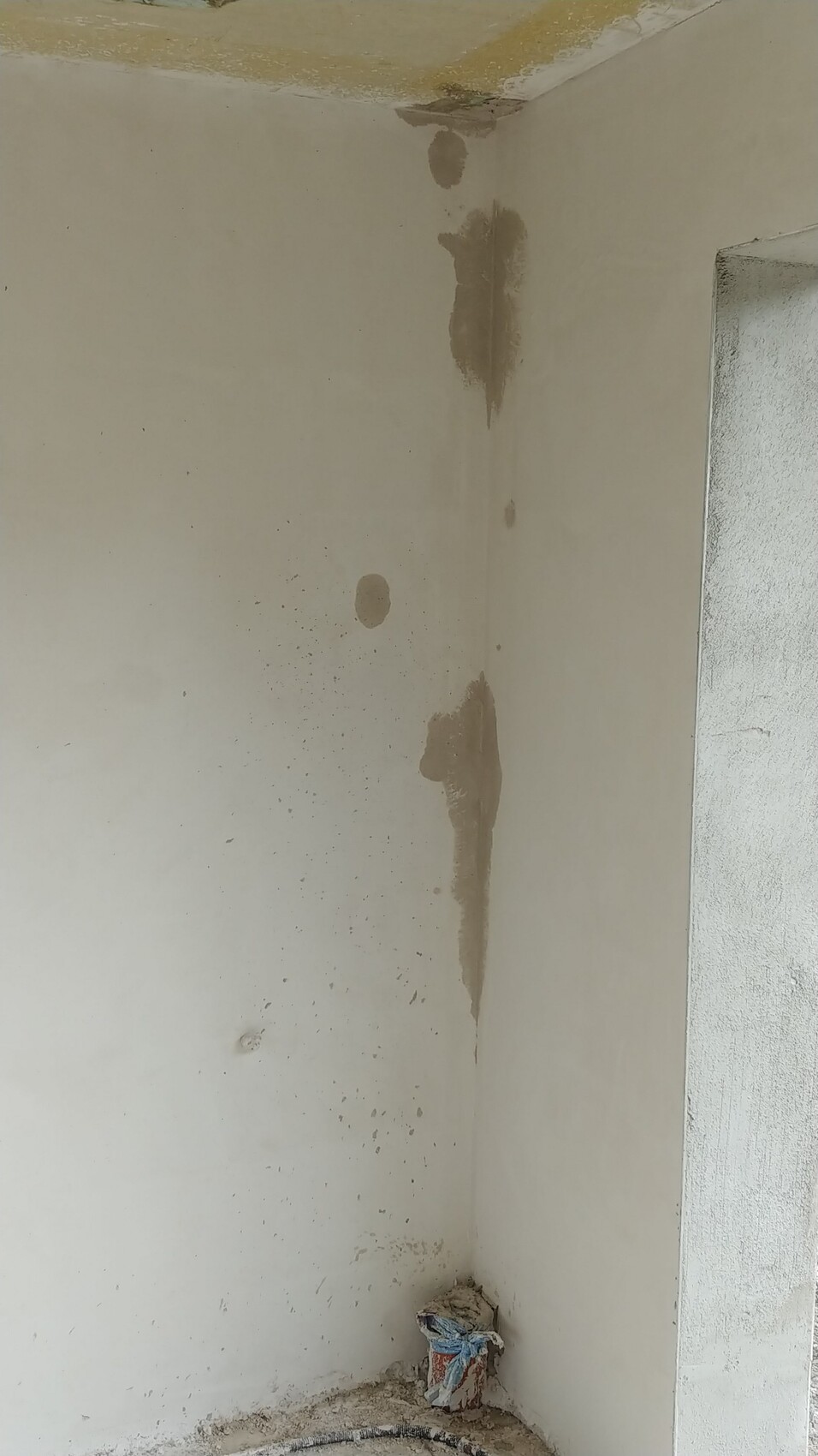 Innenwand-Ecke mit Feuchtigkeitsspuren und Putzabplatzungen, Bauabfälle am Boden