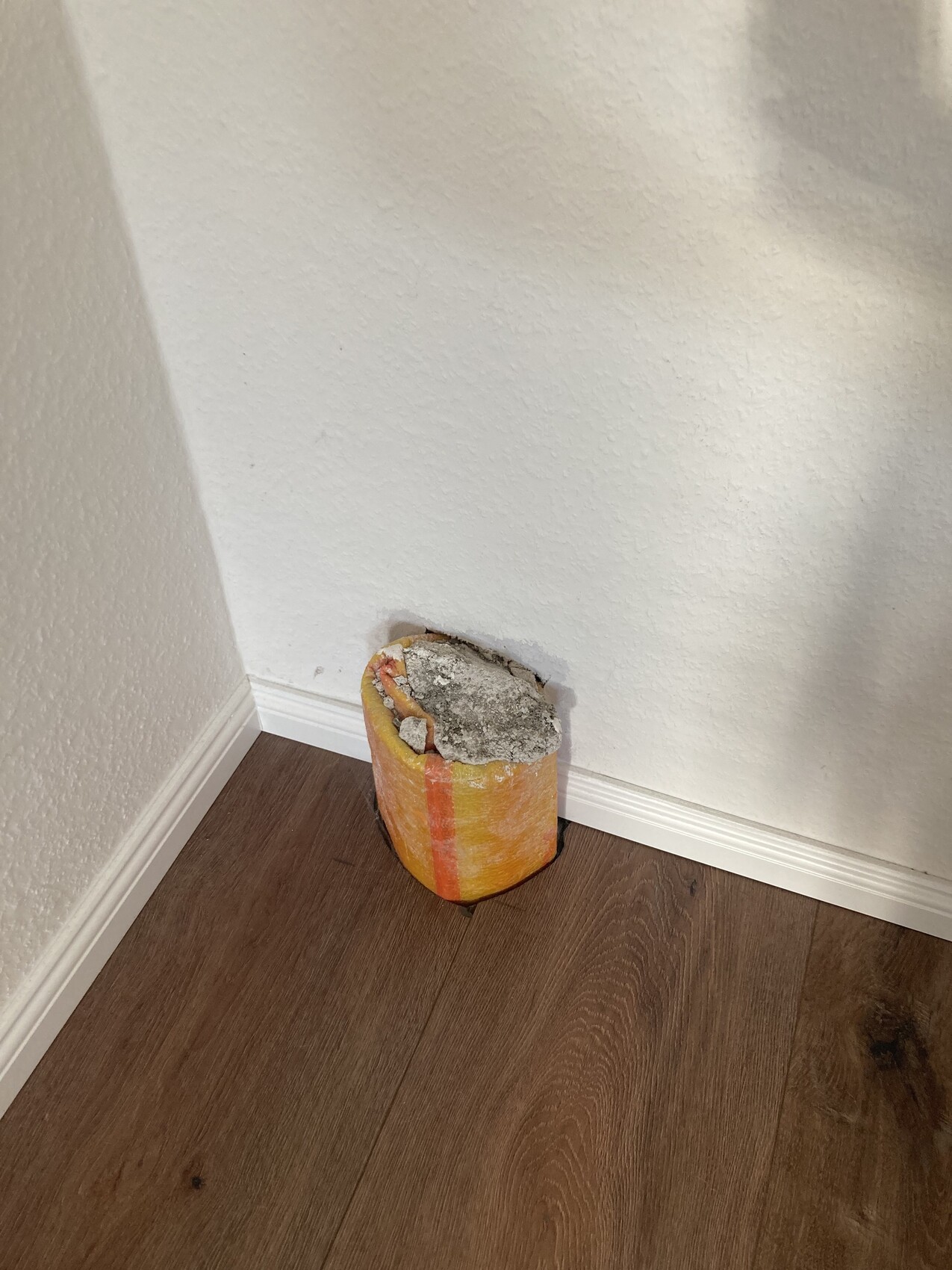 In der Ecke liegt ein oranges zylindrisches Objekt mit grauem Betonmörtel darauf.