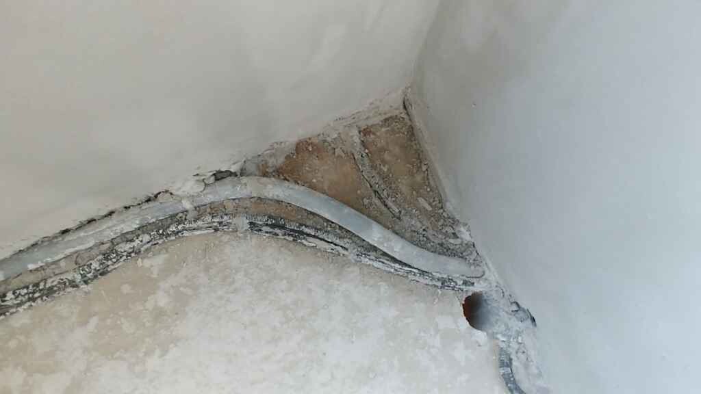 Baumaengel an Wand-Ecke: beschädigter Putz, Kabelkanal und Loch in der Wand