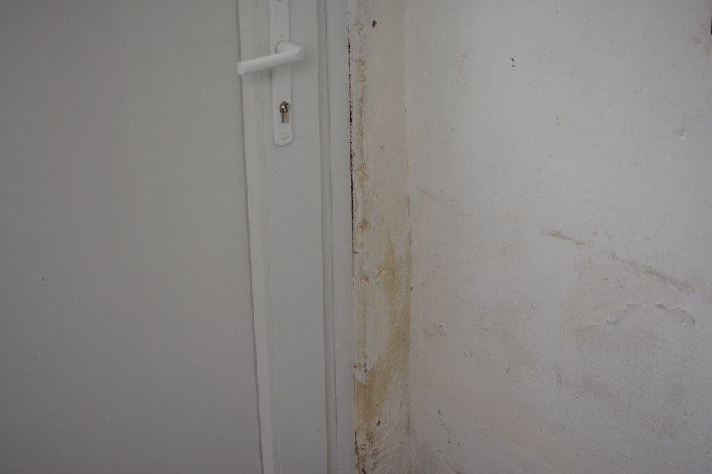 Türrahmen neben Wand mit Feuchtigkeitsschäden und abgeblättertem Putz