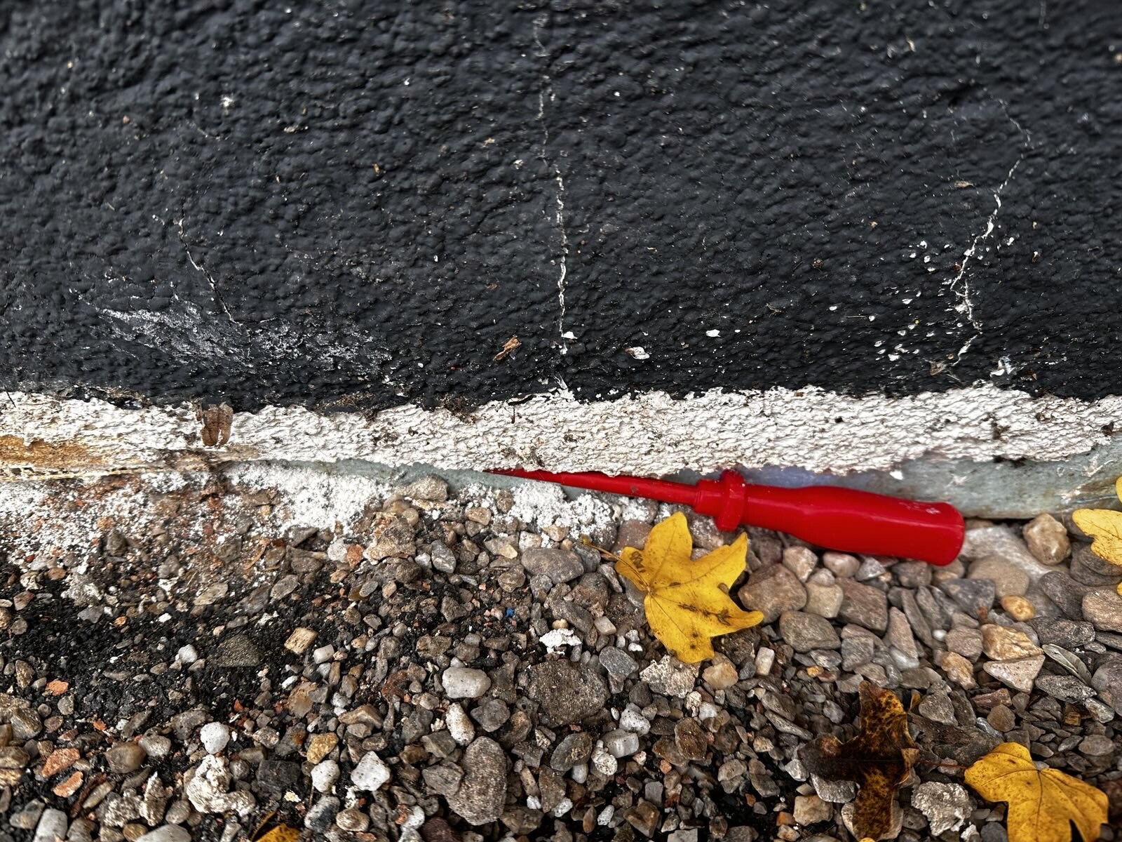 Außenwand mit schwarzer Abdichtung, weiße Fugenrisse, Kies, roter Schraubendreher