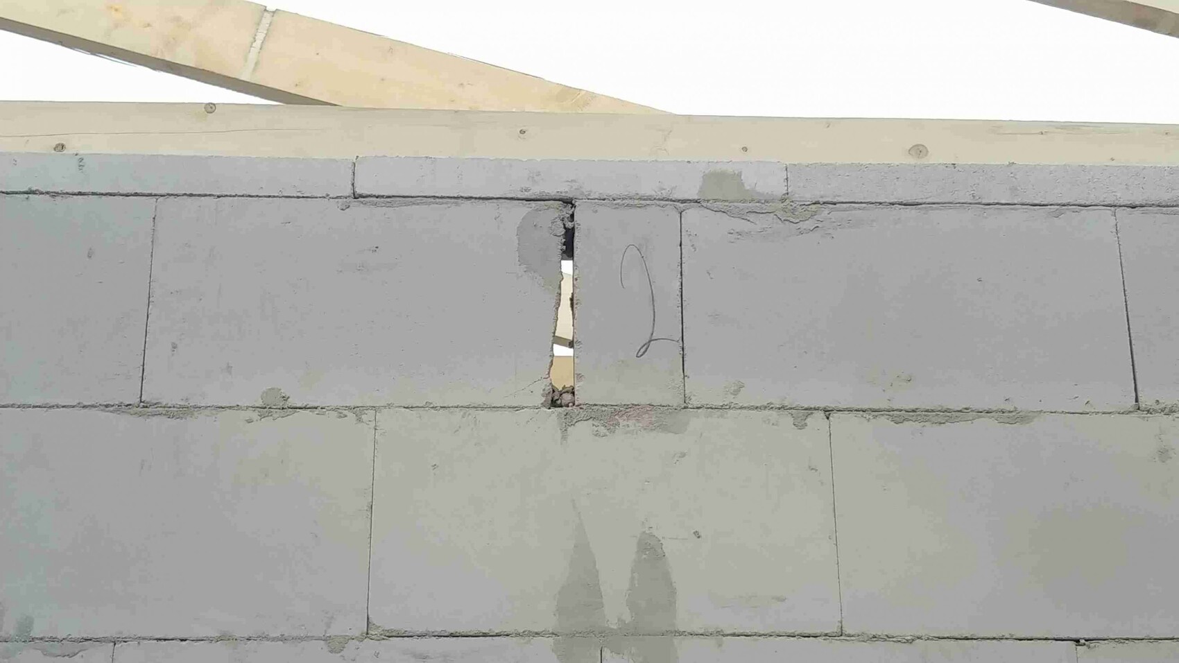 Betonblockwand mit Spalt zwischen Blöcken und Holzdachbalken sichtbar