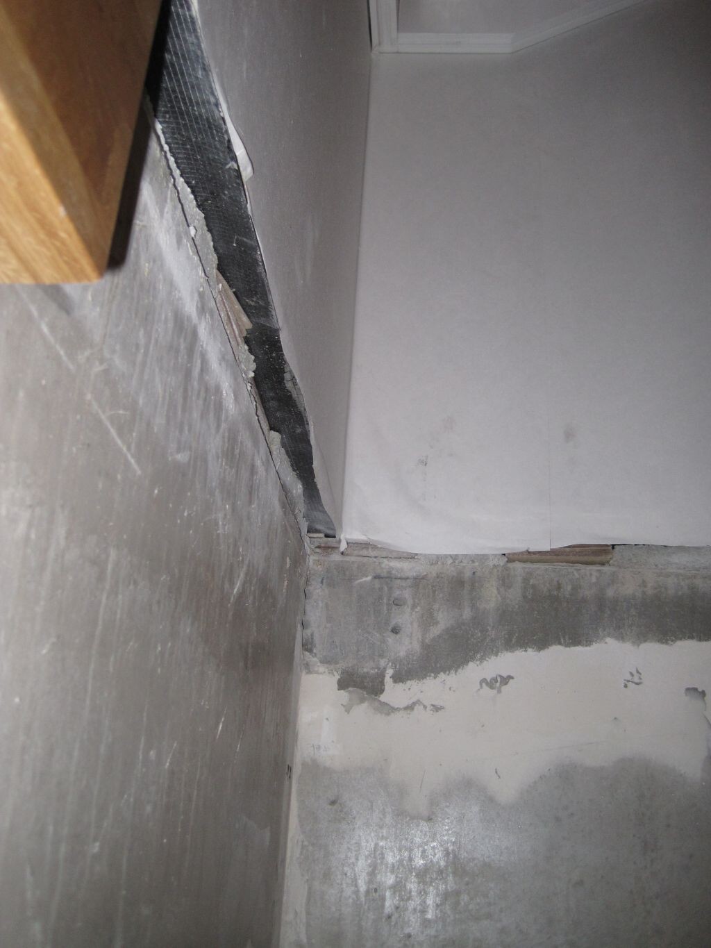 Keller-Ecke mit beschädigter Wand, abplatzendem Putz und Feuchtigkeit am Betonboden.
