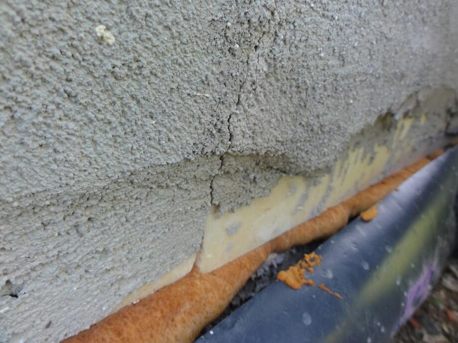 Nahaufnahme einer beschädigten Wand mit Rissen, Putz und Dämmmaterial.