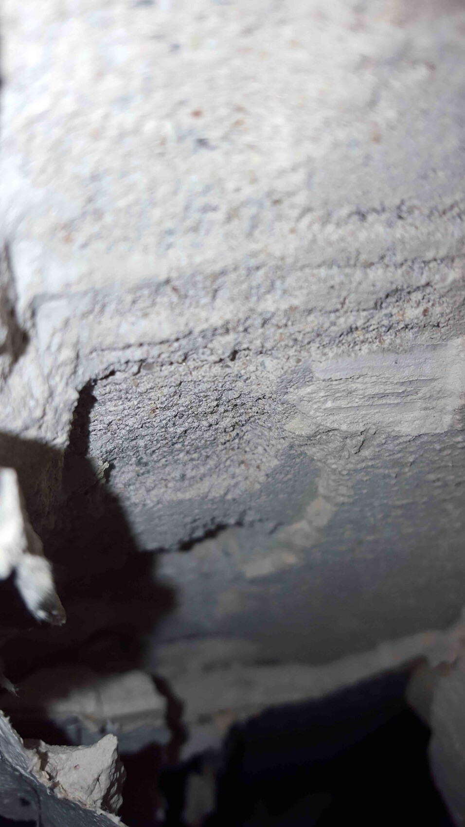 Rauer Beton mit Rissen und losem Material an einer Innenwand im Rohbau-Kellerbereich