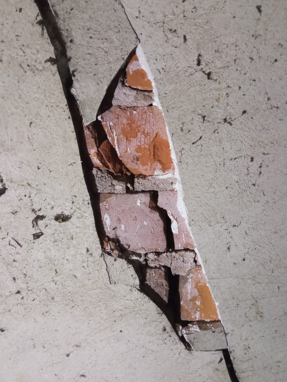Zerbrochenes rotes Ziegelstück in diagonalem Riss einer rauen Wand.