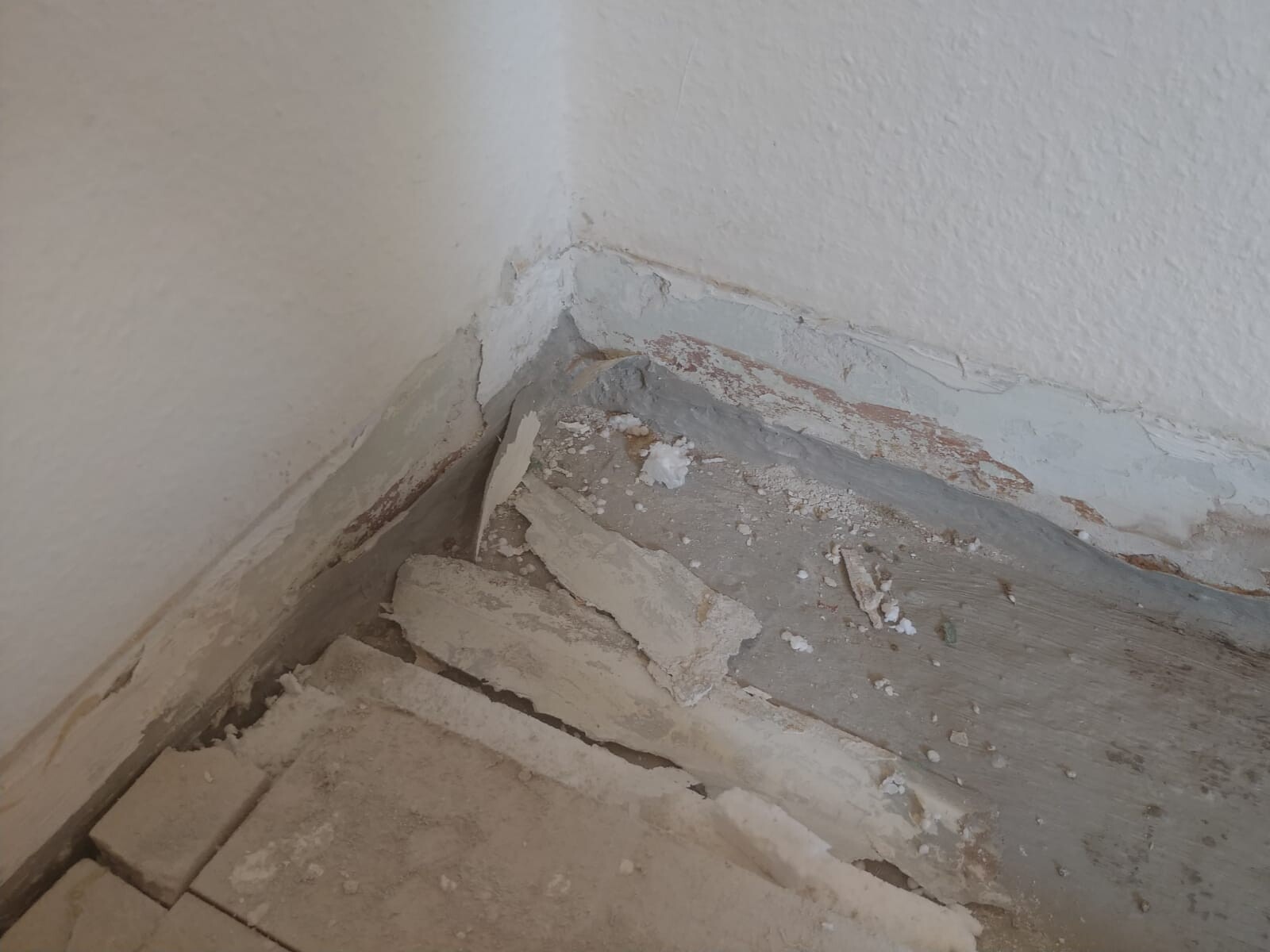 Ecke einer verputzten Wand mit abplatzendem Putz und beschädigtem Boden
