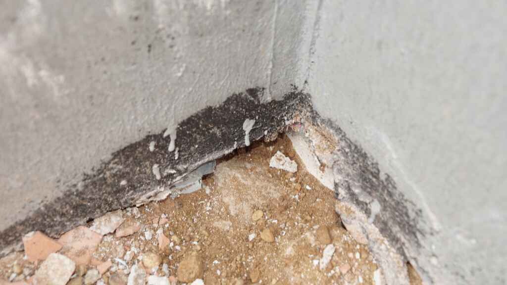 Beschädigte Betonwand mit abplatzendem Putz, Erdreich und Schutt am Boden.
