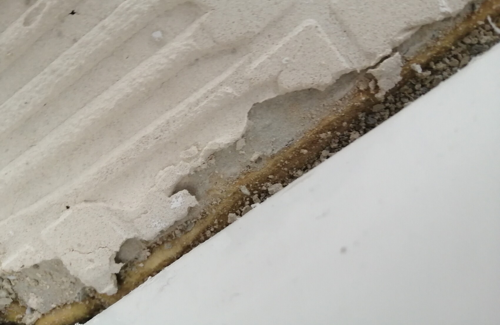 Nahaufnahme bröckelnder Putz an einer Wand mit Riss, Staub und Kies; weiße Fläche unten rechts