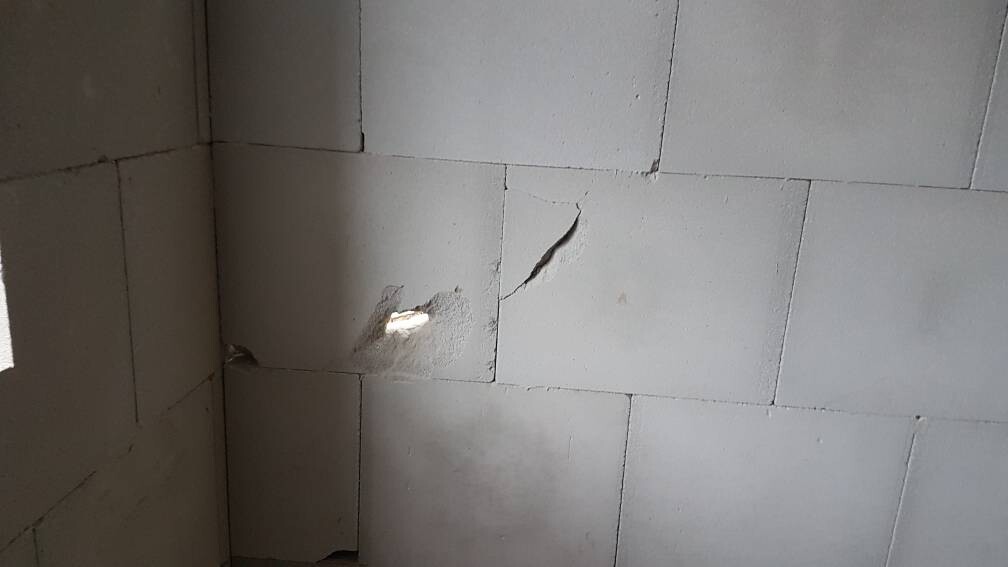 Graue Betonblockwand mit beschädigter Fläche und Loch bzw. Bruchstelle, Licht durchbricht die Wand.
