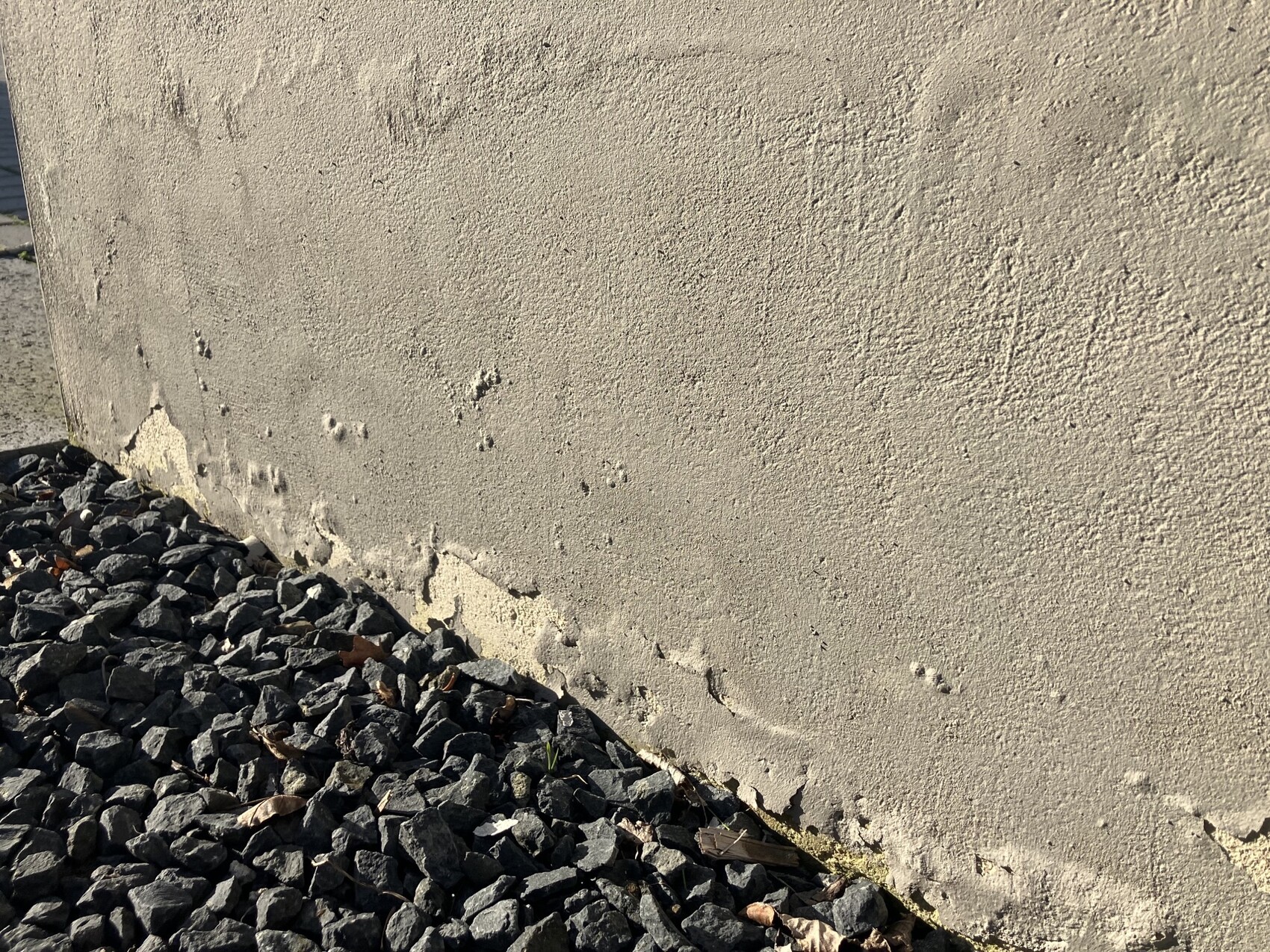 Beige Wand mit rissigem Putz; unten ein Haufen grauer Steine und Kies.