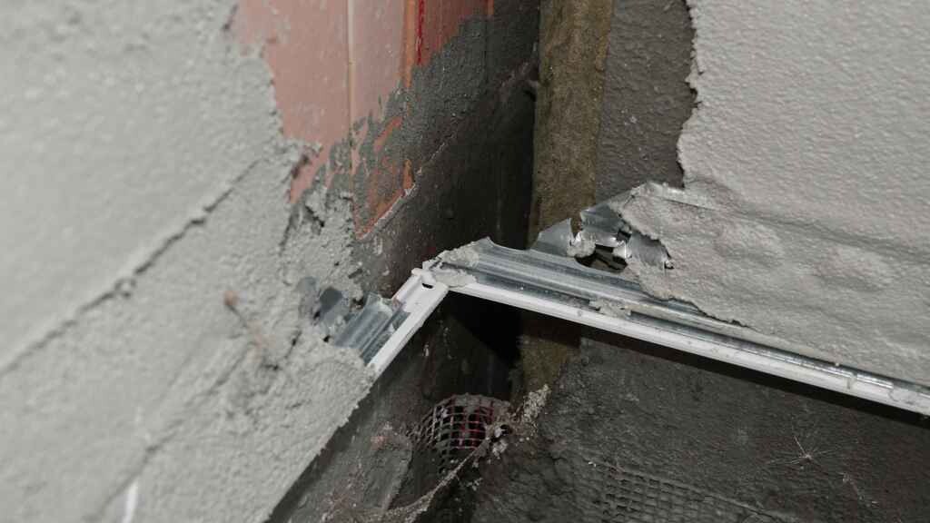 Innenwand mit Putzabplatzungen, Beton und Metallrahmen - Baumaengel-Szene