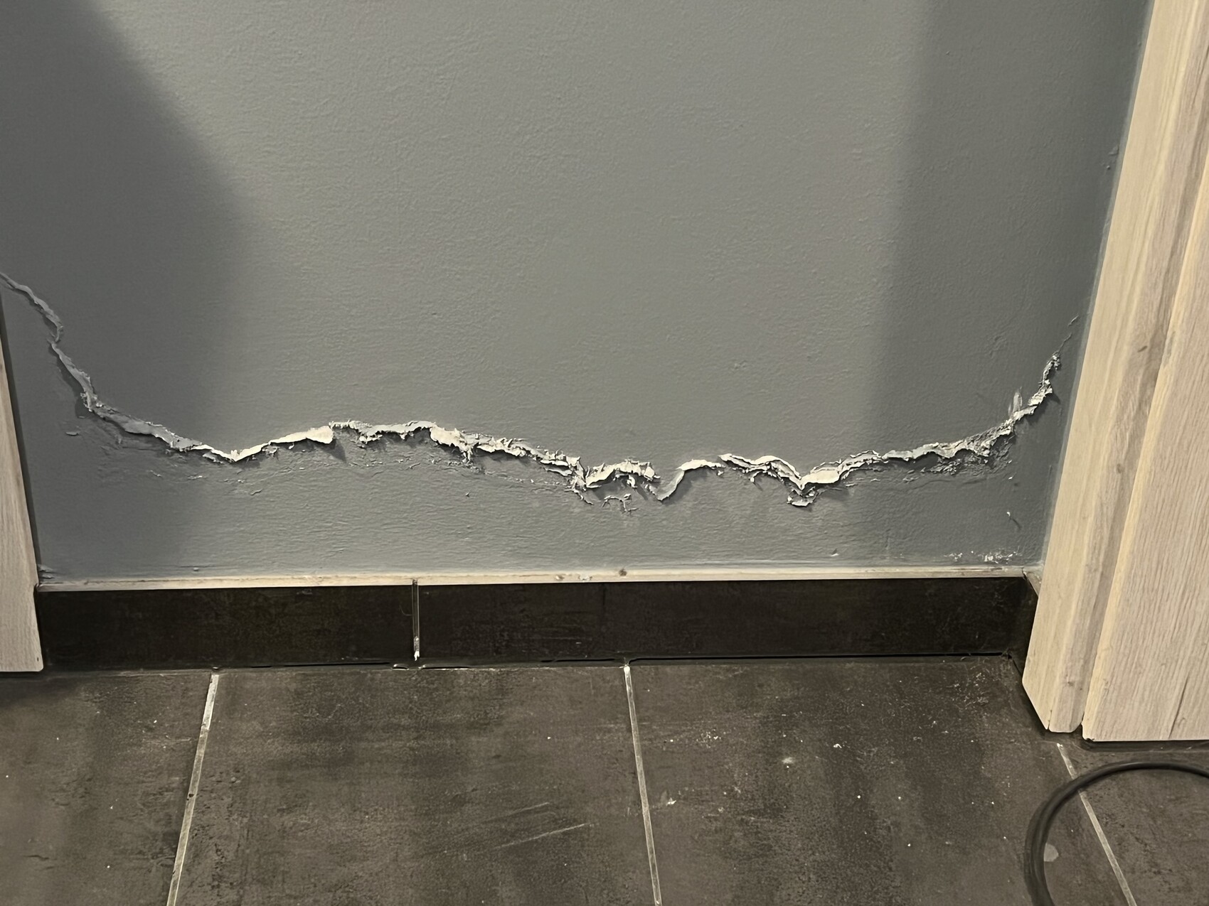 Beschädigte Innenwand mit abblätternder Putzschicht über Fliesenboden