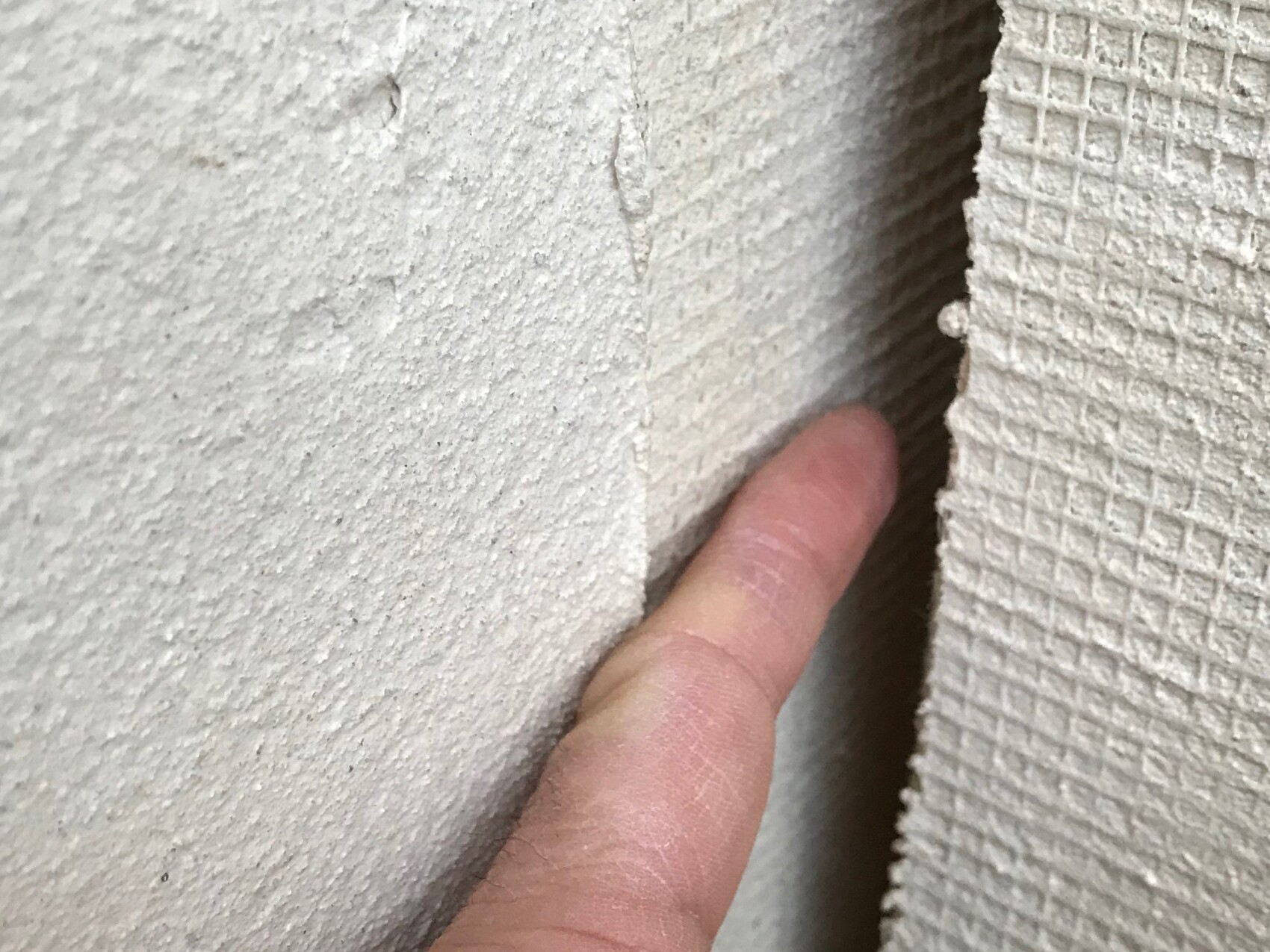 Finger zeigt feine Risse an rauer Wandfuge, Hinweis auf Baumangel