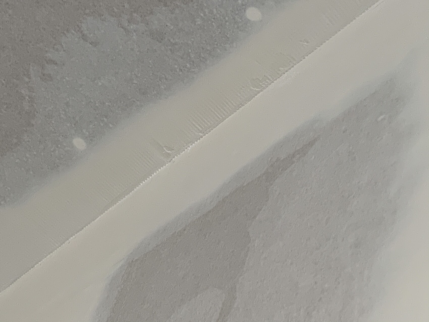 Nahaufnahme eines weißen Randstreifens auf grobem grauem Untergrund, diagonal angeordnet.