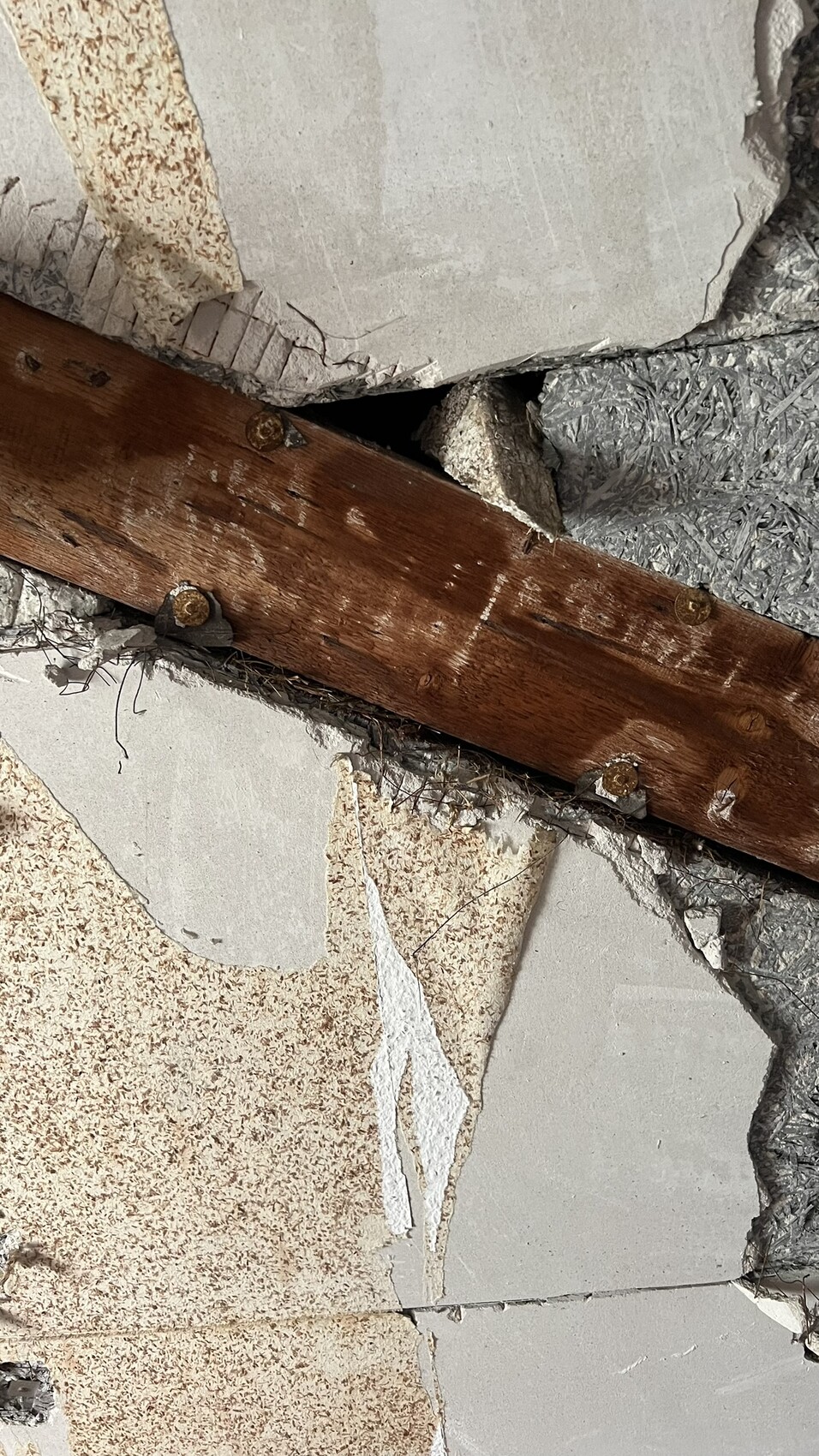 Nahaufnahme einer beschädigten Wandkonstruktion mit Holzbalken, Putz und Dämmmaterial.