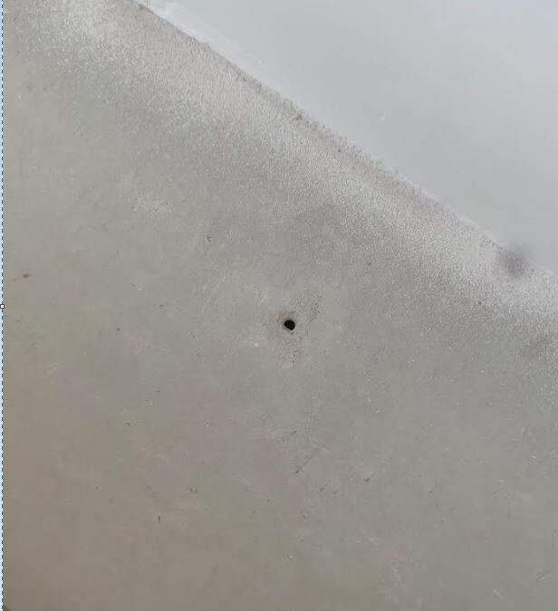 Nahaufnahme einer hellgrauen Wandfläche mit kleinem schwarzen Loch.