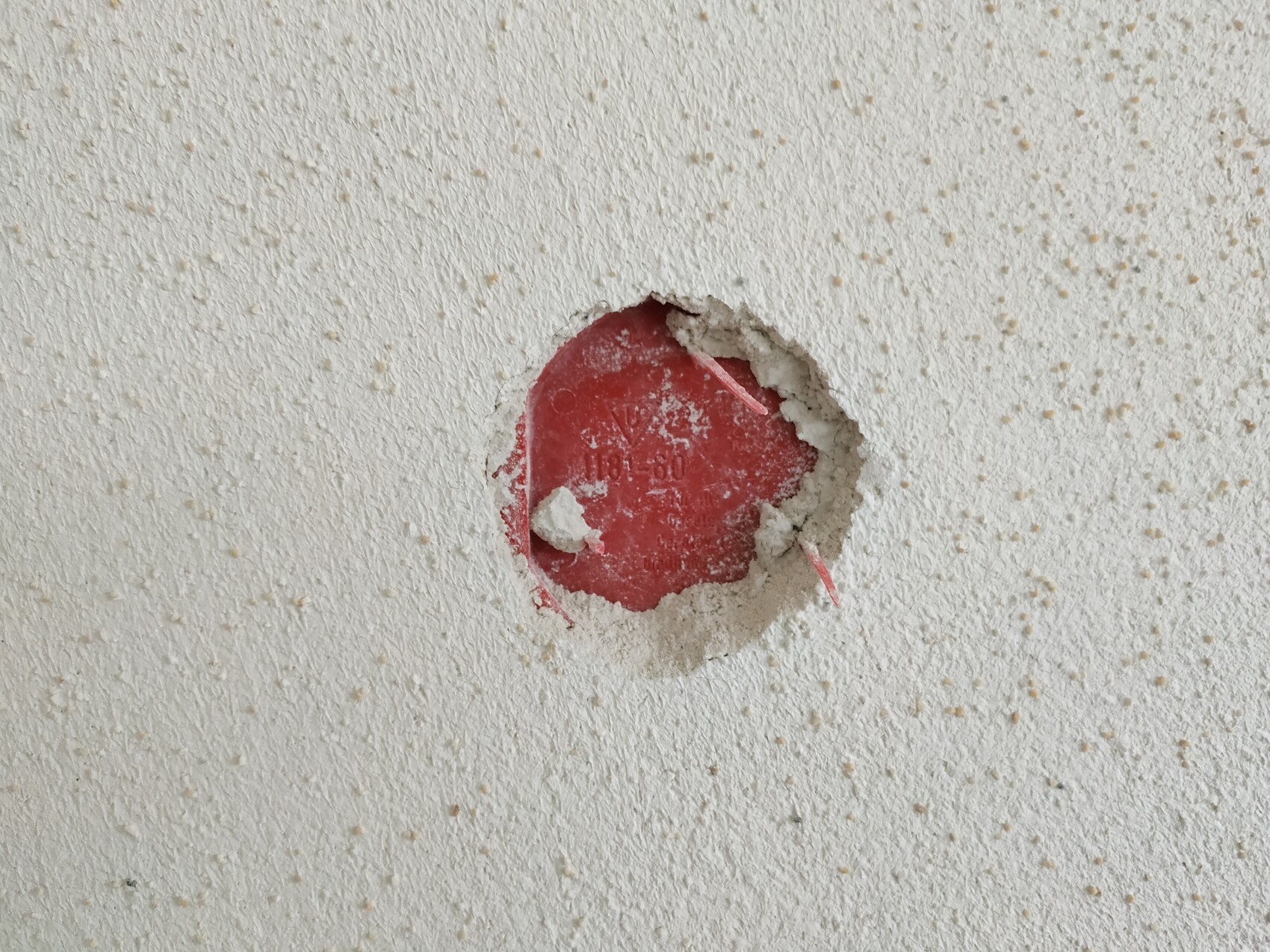 Durchbruch in weißer Wand zeigt roten runden Deckel eines Rohrsystems, umgeben von losem Putz.