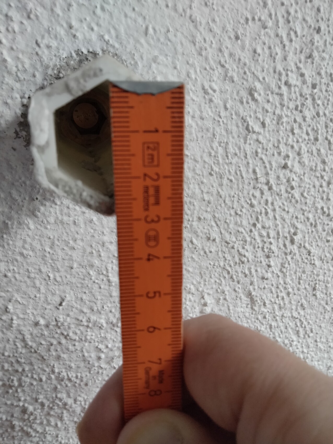 Nahaufnahme eines orangefarbenen Maßbands, das eine Wandöffnung misst; Hand hält es.