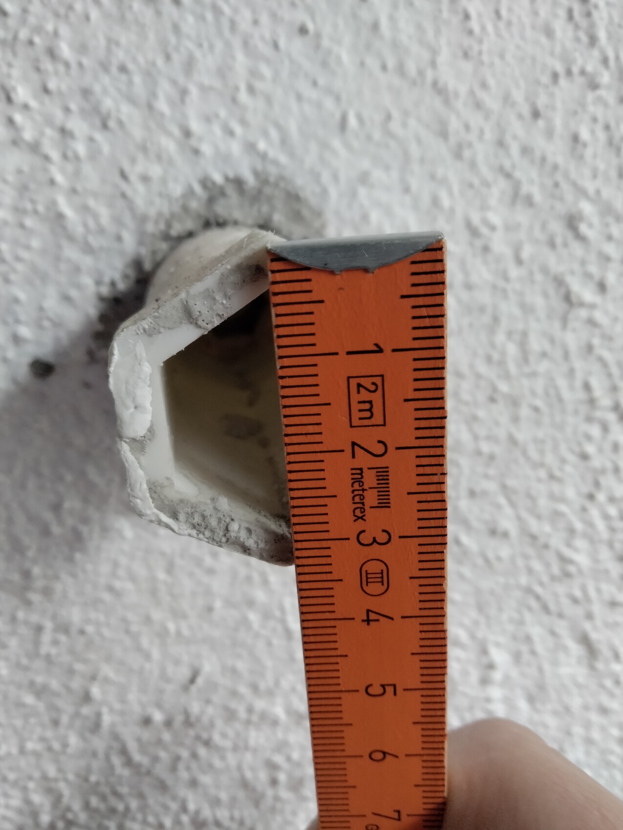 Loch in weiß verputzter Wand, von Putz umgeben; daneben orangefarbener Messstab mit Skalen.