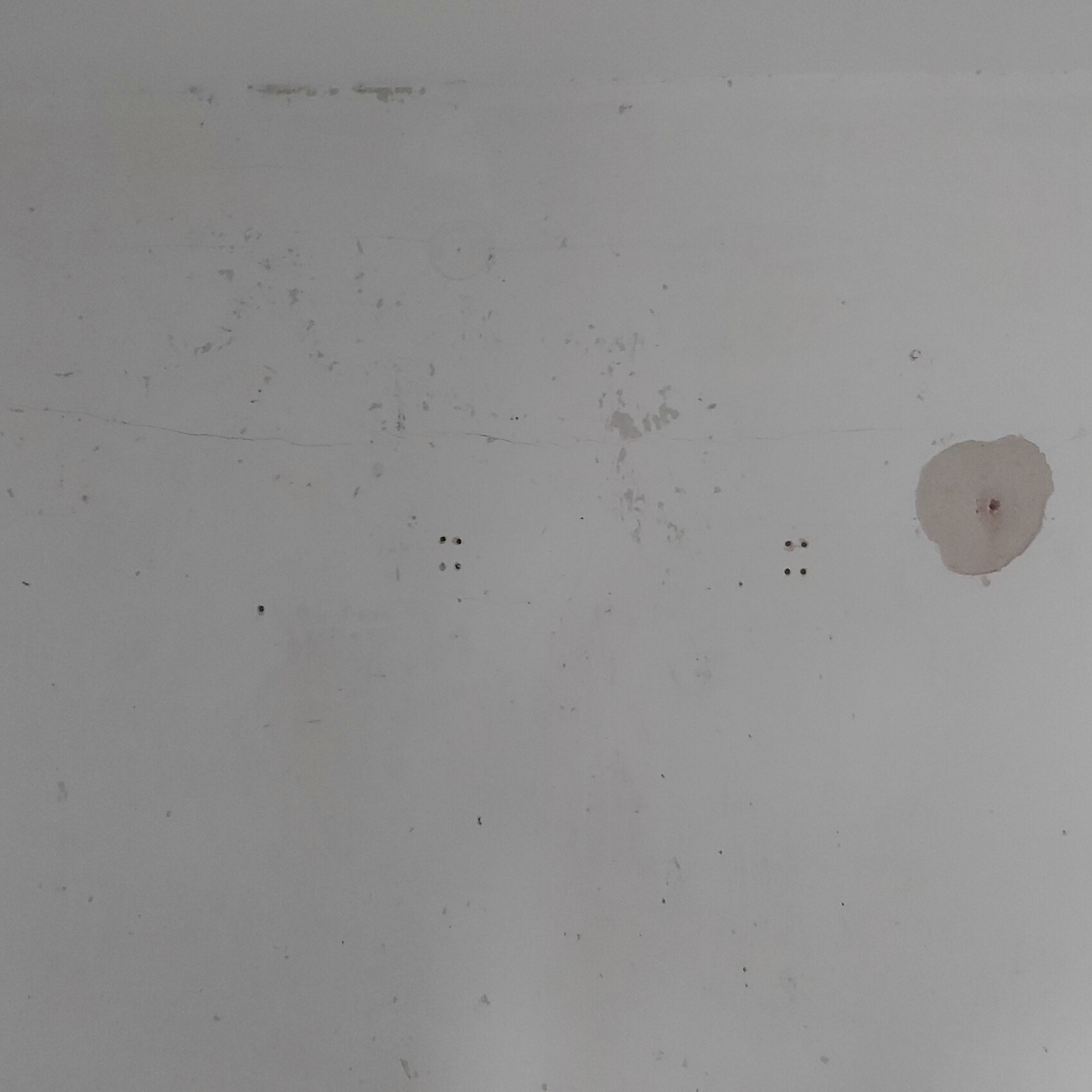 Weiße Wand mit Spachtelputz-Flecken und kleinen Löchern, Baufehler sichtbar