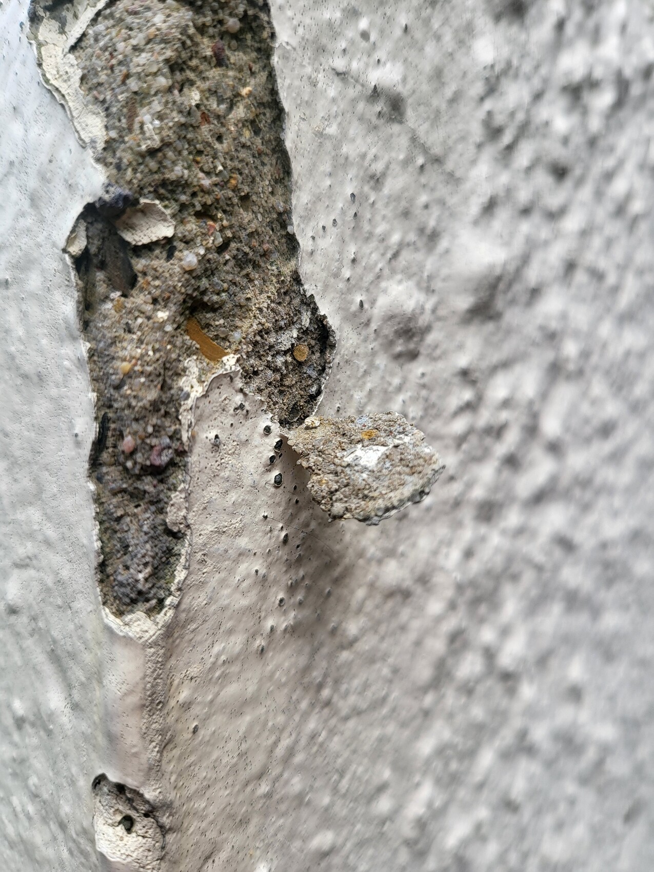 Nahaufnahme einer abplatzenden Betonwand mit freiliegendem Gestein, Kies und Zement.