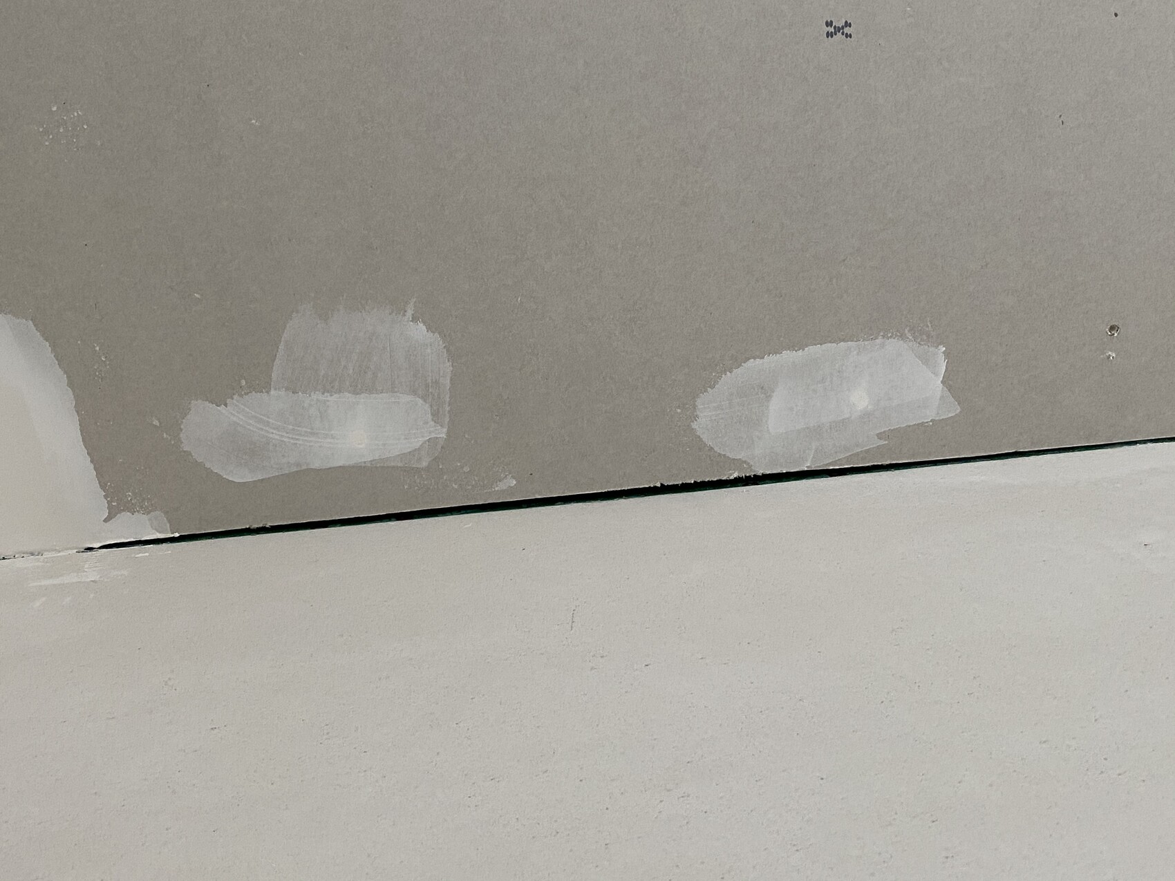 Zwei ovale, weiße Spachtel-Patches an einer grauen Wand über dem Boden.