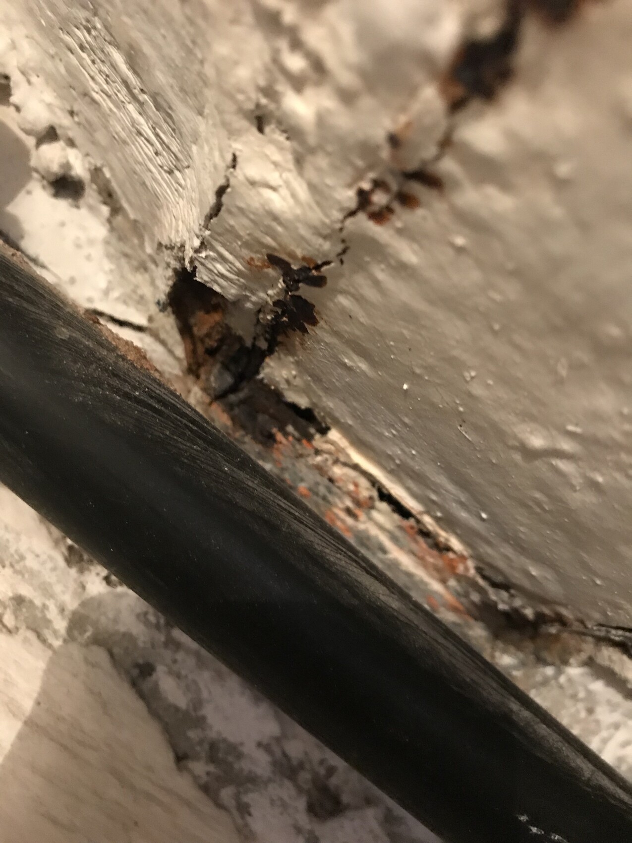 Nahaufnahme einer rauen Wand mit abgeplatztem Putz, Rissen und Rostflecken, durch Rohrleitung geteilt