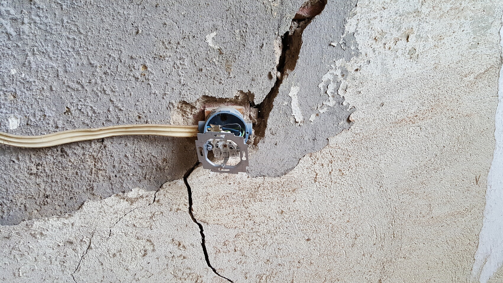 Rissige Wand mit offener Elektro-Dose und verlaufenden Kabeln.