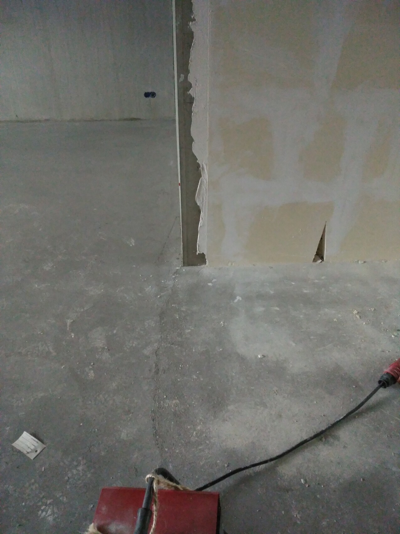 Unfertige Innenwand mit abgeplatztem Putz, rauer Boden und Baukabel