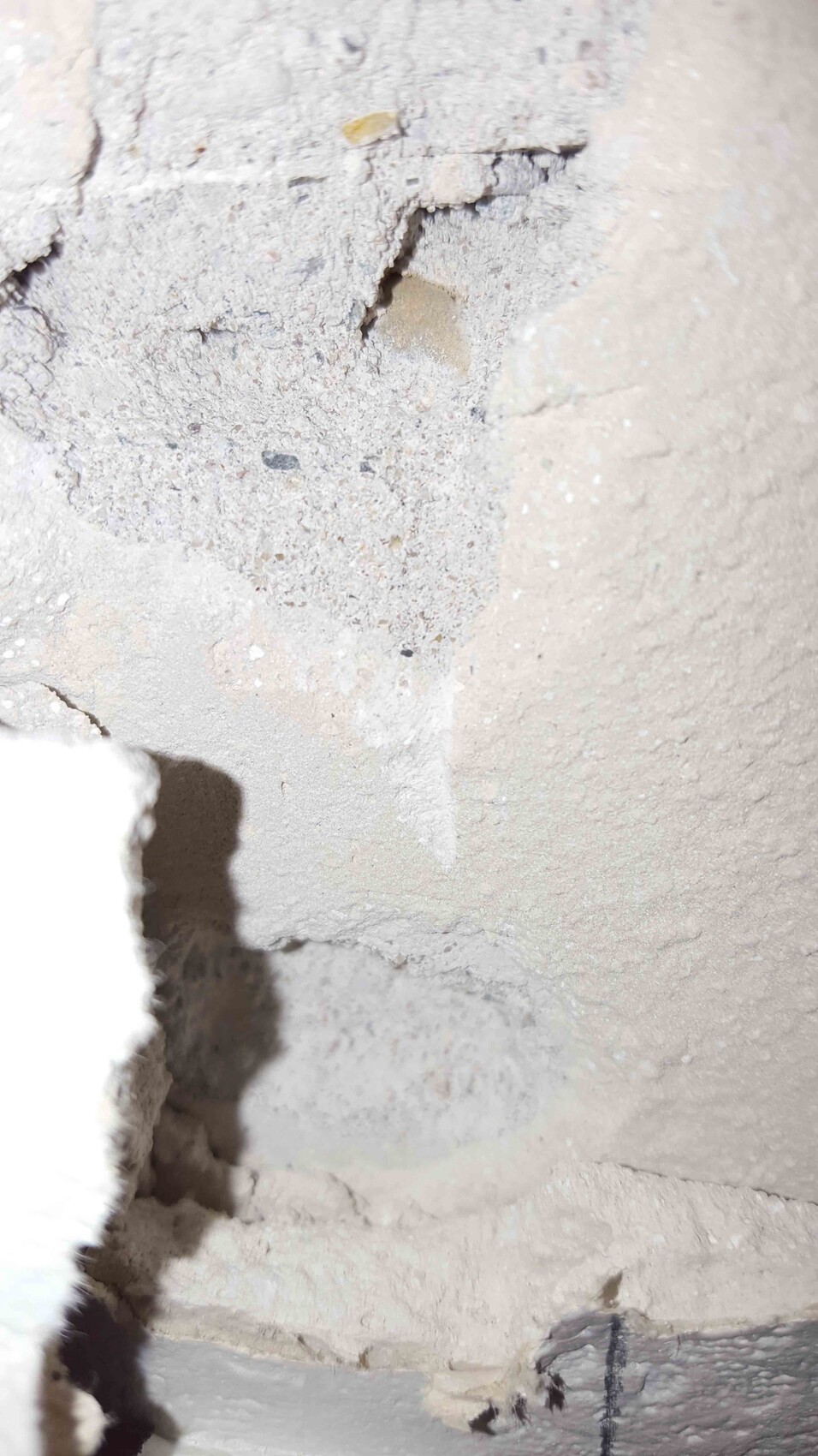 Nahaufnahme einer rauen Betonwand mit bröckeligem Putz, Rissen und Staub auf einer Baustelle.