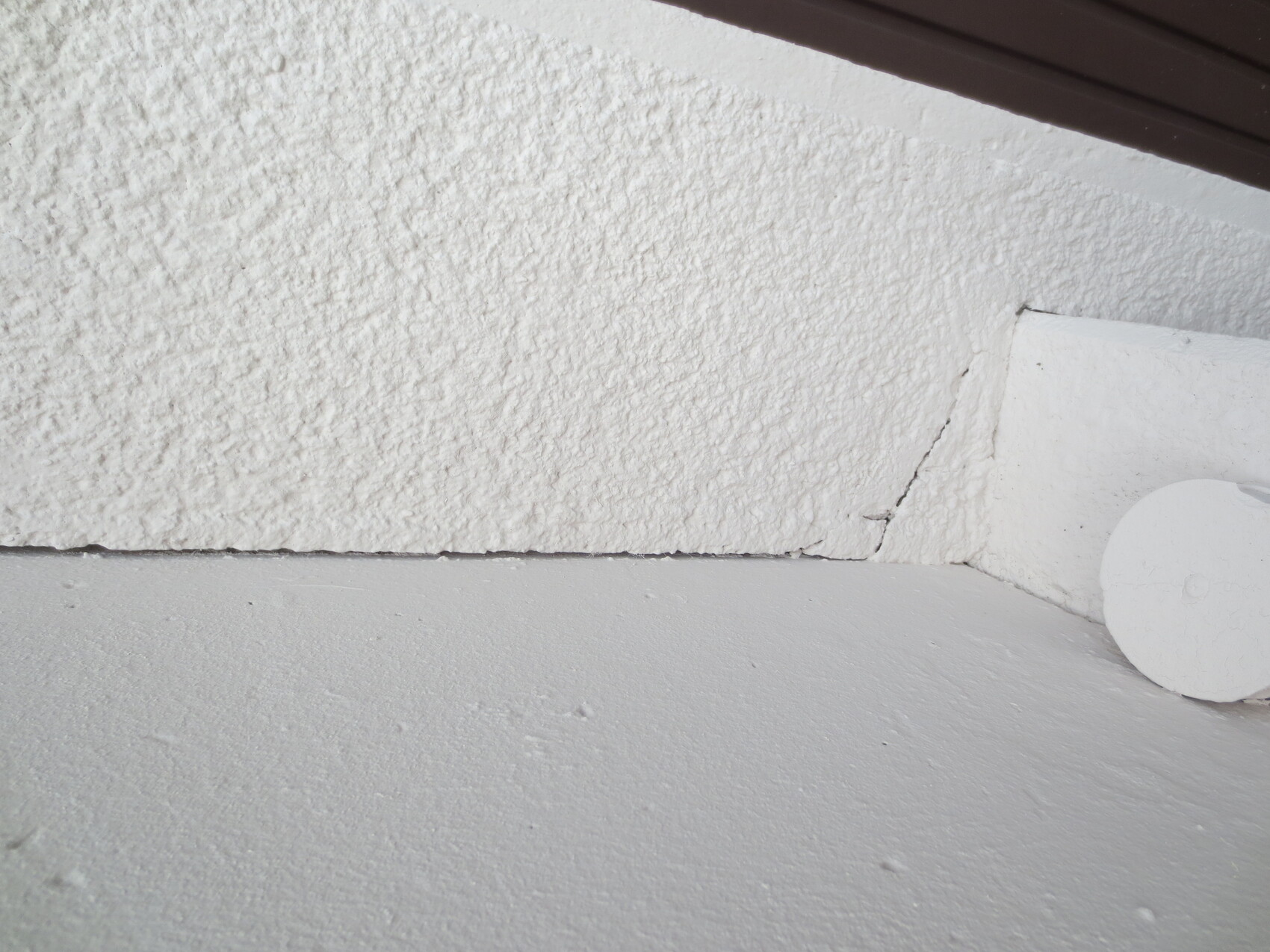 Außenwand-Eckbereich: glatte graue Fläche links, grobtexturierte weiße Fläche rechts, Riss unten.