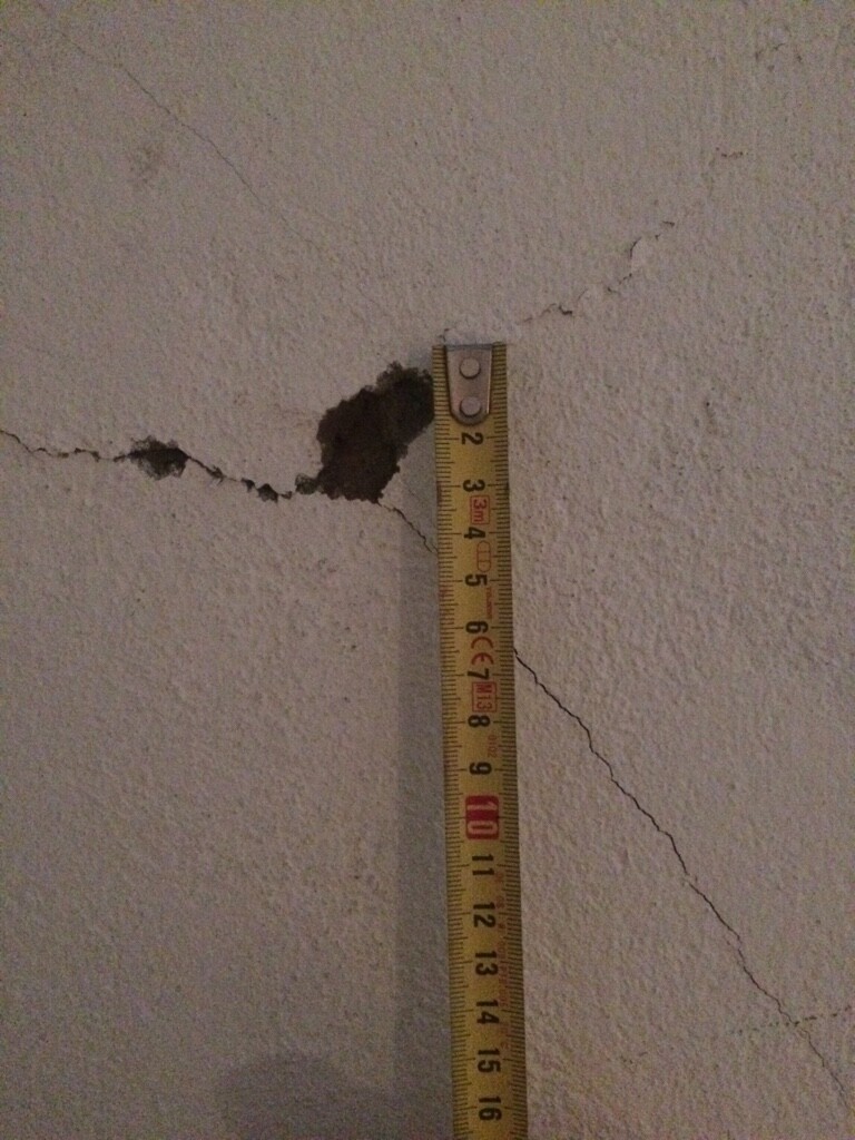Wand mit sichtbarem Riss, Maßband zeigt Schadensausmaß
