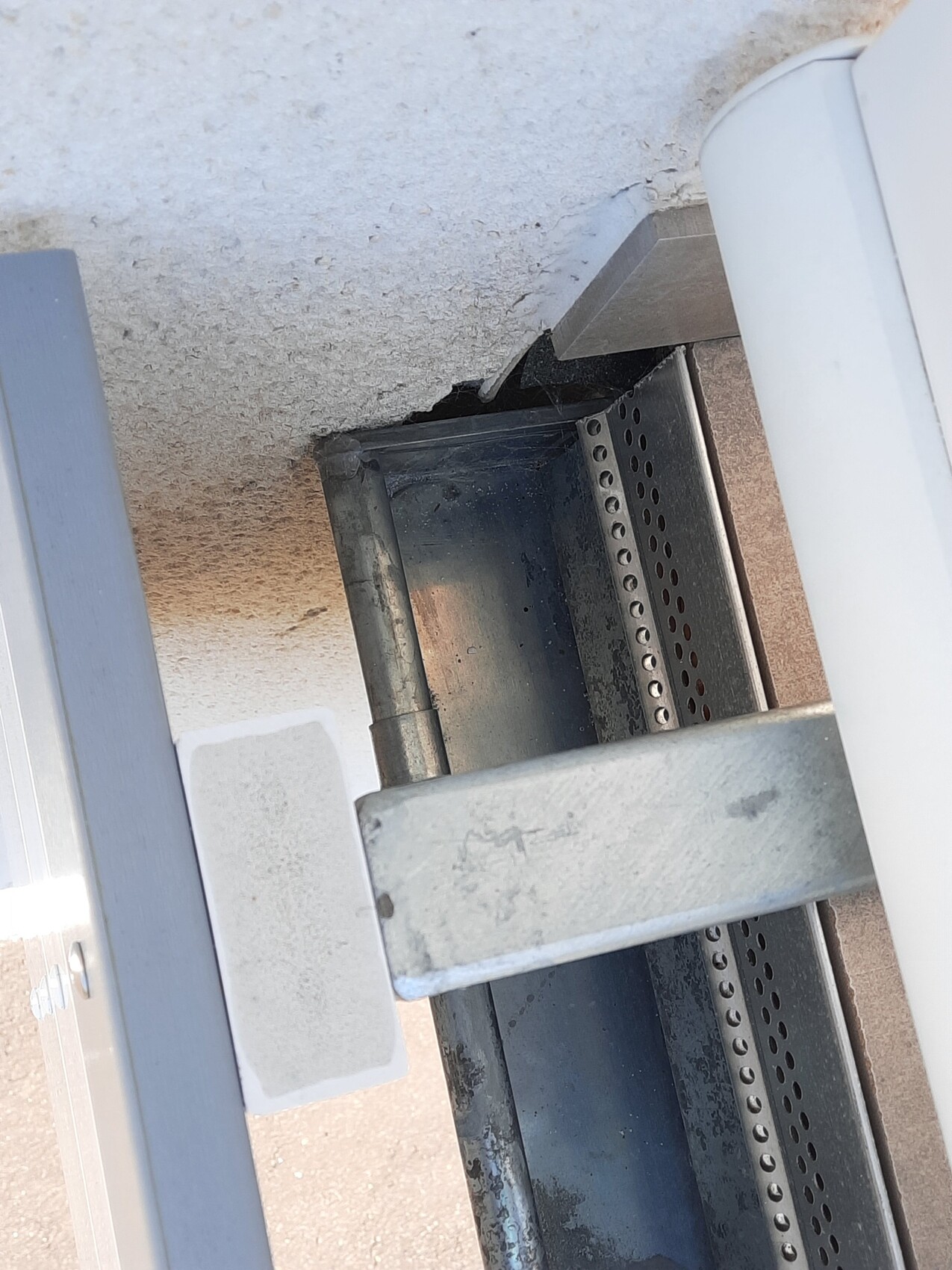 Nahaufnahme einer Lochblech-Schiene in einer Wandöffnung neben einer rissigen Betonwand.