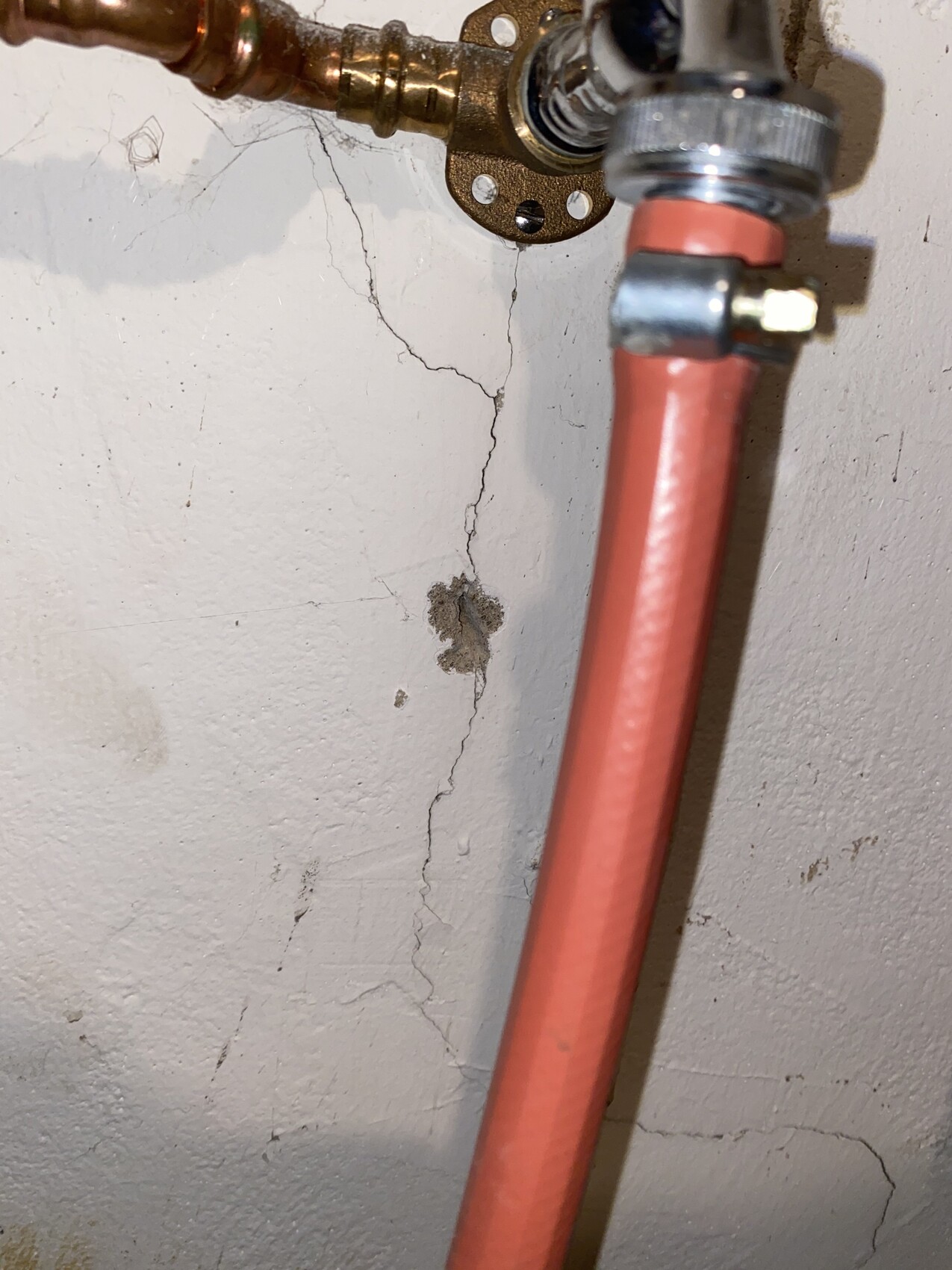 Rotes PEX-Rohr mit Absperrventil vor einer rissigen Wand und Kupferleitungen.