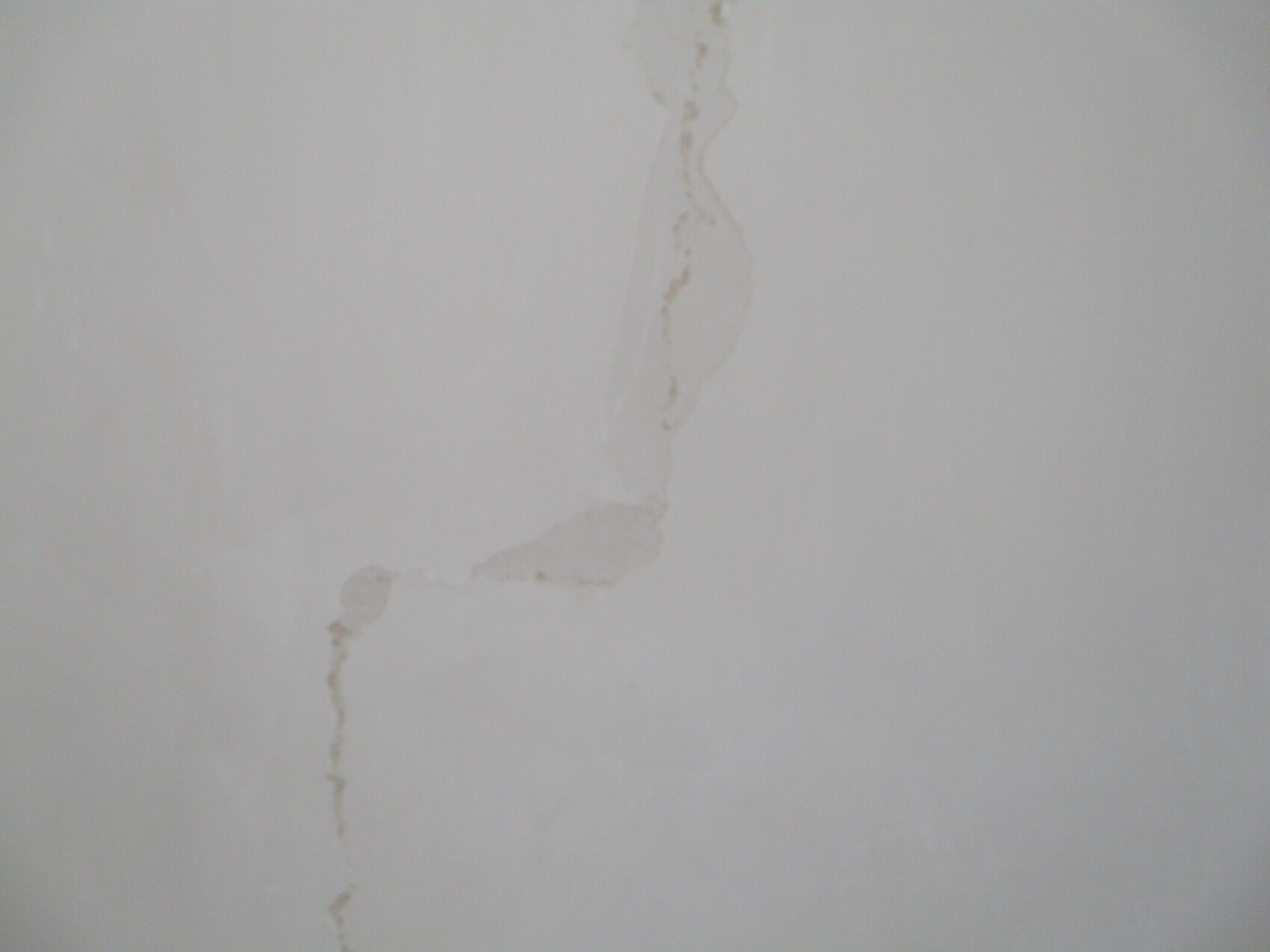 Weiße Wand mit einem bräunlichen, geschwungenen Riss von oben nach unten.