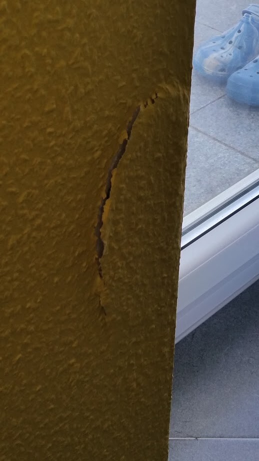 Gelbe Wand mit Riss in Putzoberflaeche neben Fenster