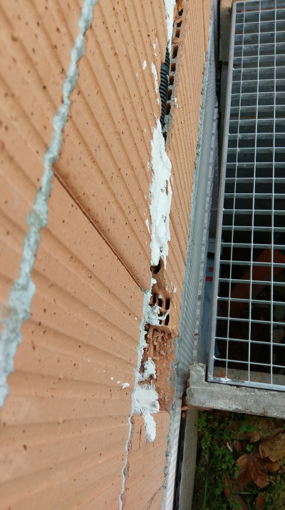Außenwand aus Ziegel mit Rissen und abgeplatztem Putz neben Metallgitter