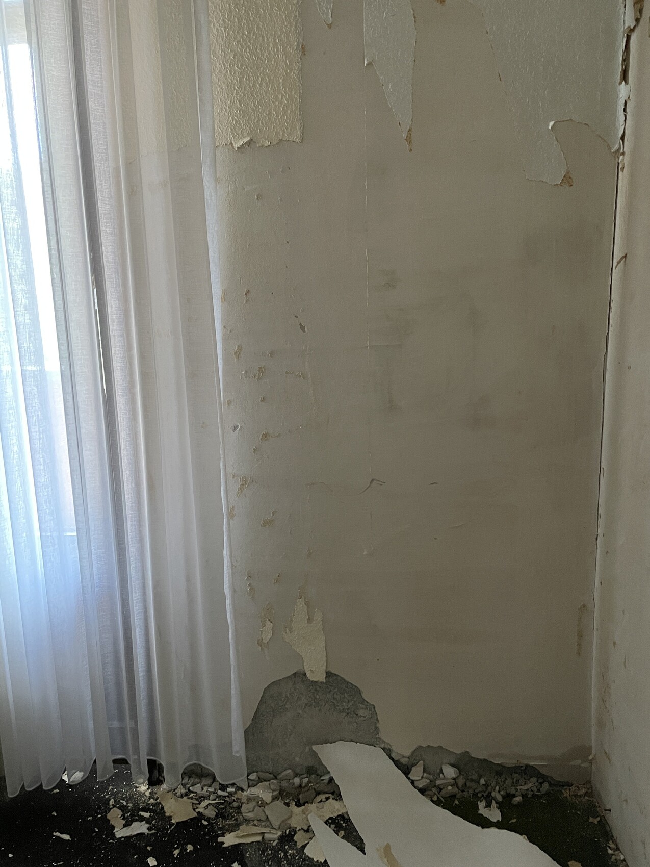 Ecke einer Wand mit abblätternder Farbe, Putzbruch unten, Trümmer auf dem Boden.