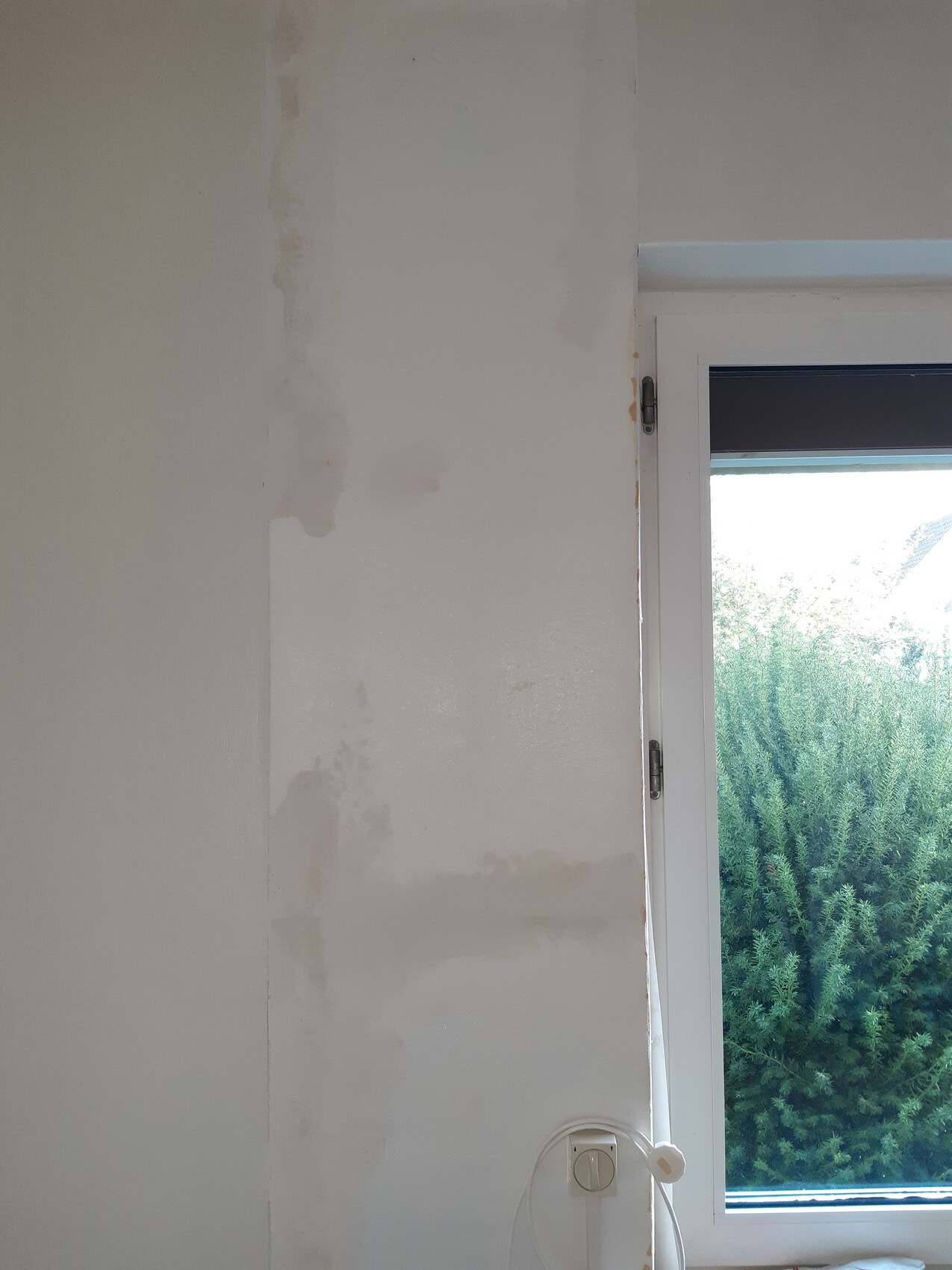Weiße Innenwand mit ungleichmäßig verputzten Flächen neben einem Fenster.